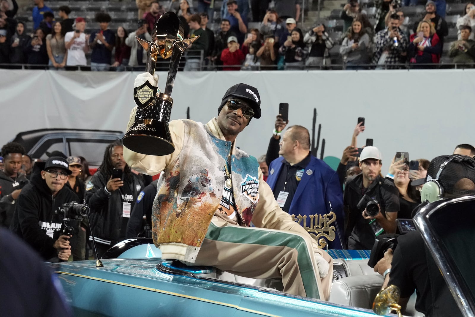 Rapper Snoop Dogg, center, arrives with the trophy after Miami (Ohio) defeated Colorado State in the Arizona Bowl NCAA college football game, Saturday, Dec. 28, 2024, in Tucson, Ariz. (AP Photo/Rick Scuteri)