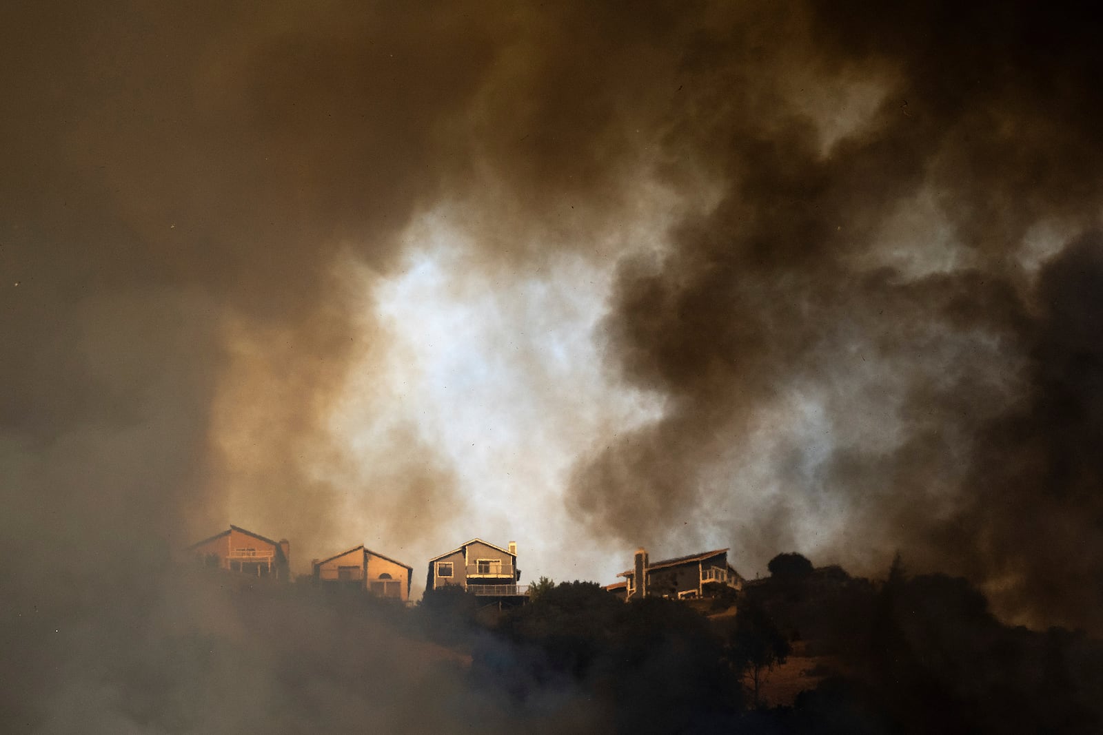 Smoke rises above homes as a grass fire burns near Interstate 580 in Oakland, Calif., Friday, Oct. 18, 2024. (AP Photo/Noah Berger)