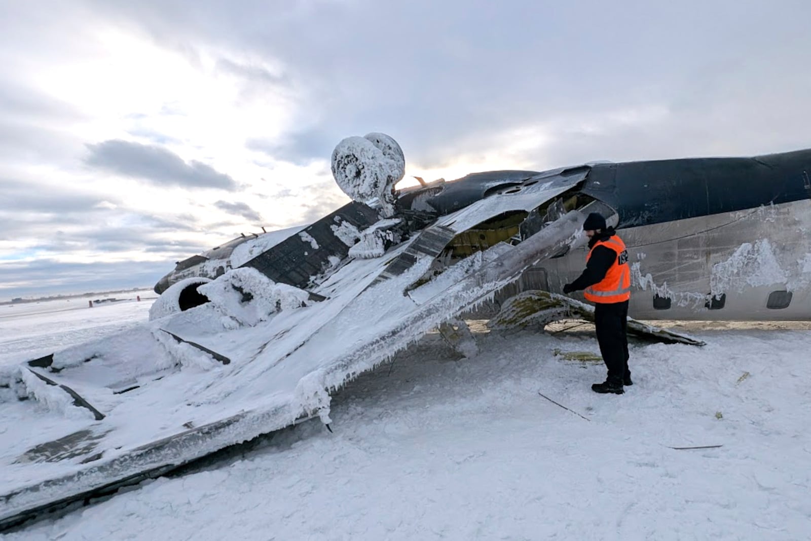 In this image provided by the National Transportation Safety Board, an investigator examines the wreckage of a Delta Air Lines jet, Wednesday, Feb. 19, 2025, that burst into flames and flipped upside down as it tried to land on Feb. 17, at Toronto Pearson International Airport in Mississauga, Ontario. (National Transportation Safety Board via AP)