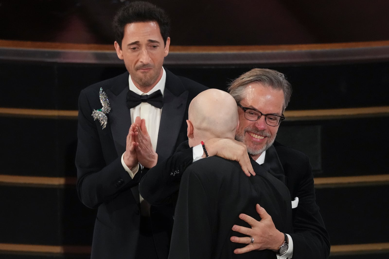 Adrien Brody, left, and Guy Pearce, right, congratulate Daniel Blumberg, center, for winning the award for best original score for "The Brutalist" during the Oscars on Sunday, March 2, 2025, at the Dolby Theatre in Los Angeles. (AP Photo/Chris Pizzello)