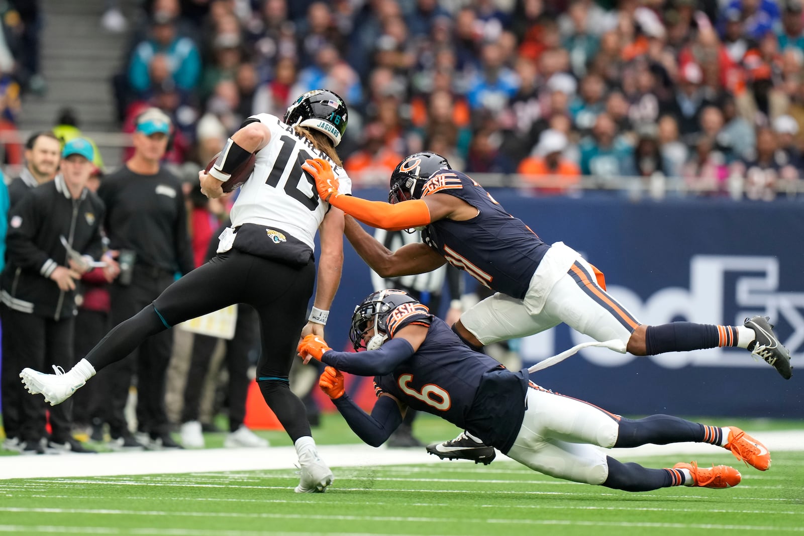 Jacksonville Jaguars quarterback Trevor Lawrence (16) is tackled by Chicago Bears safety Kevin Byard III (31) and cornerback Kyler Gordon (6) during an NFL football game at the Tottenham Hotspur stadium between the Jacksonville Jaguars and Chicago Bears in London, Sunday, Oct. 13, 2024. (AP Photo/Alastair Grant)