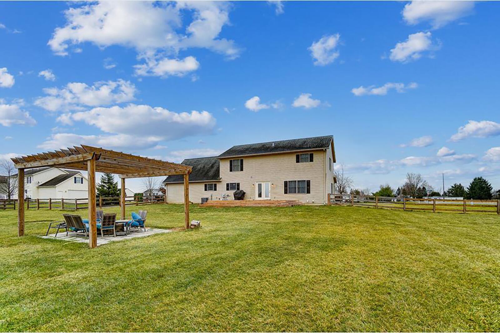 The rear of the home features a wood deck with surrounding steps, a pergola over a built-in firepit and open backyard.