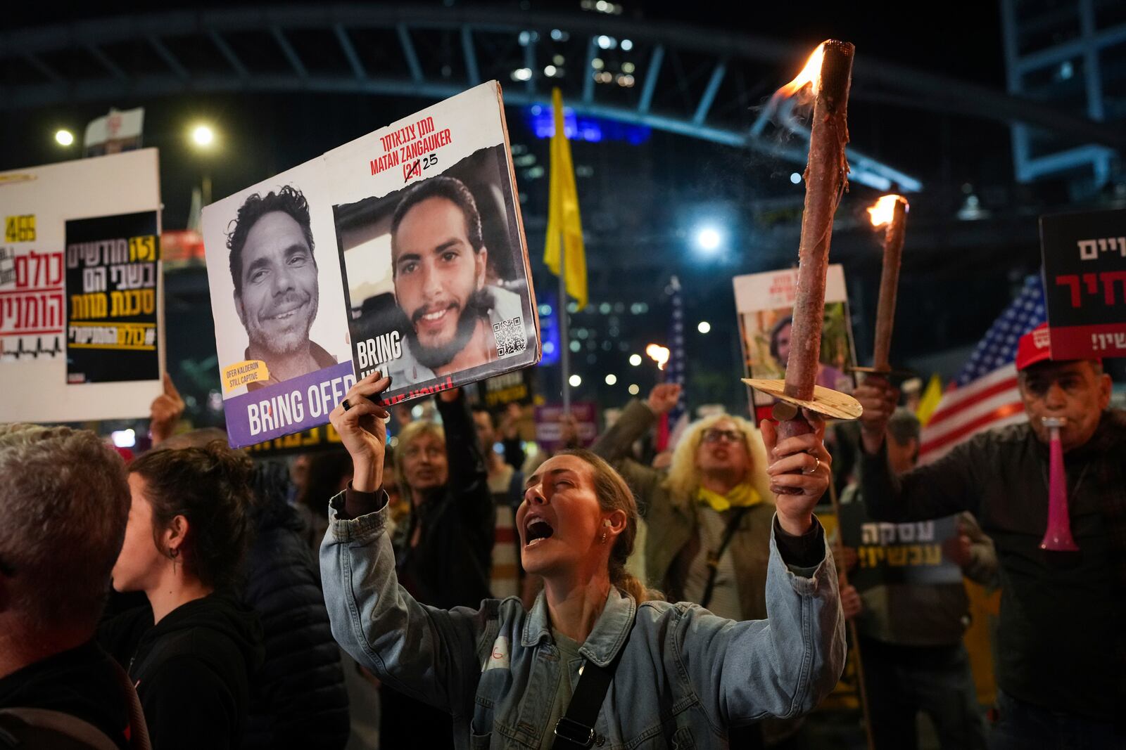 Demonstrators hold torches during a protest calling for the immediate release of the hostages held in the Gaza Strip by the Hamas militant group in Tel Aviv, Israel, on Monday, Jan. 13, 2025. (AP Photo/Ohad Zwigenberg)