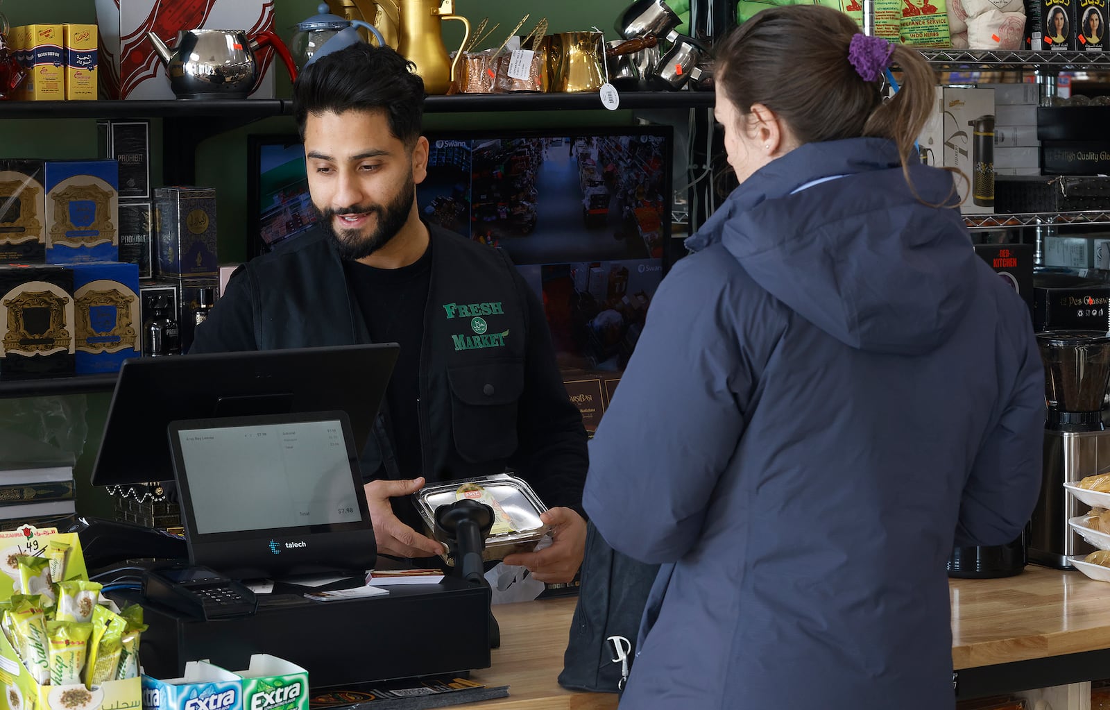 Muhajer "Amir" Almosawi, owner of the Fresh Halal Market, helps a shopper to checkout Wednesday,  Jan. 15, 2025. The market moved to a new location on Lyons Road in Washington Township. MARSHALL GORBY\STAFF