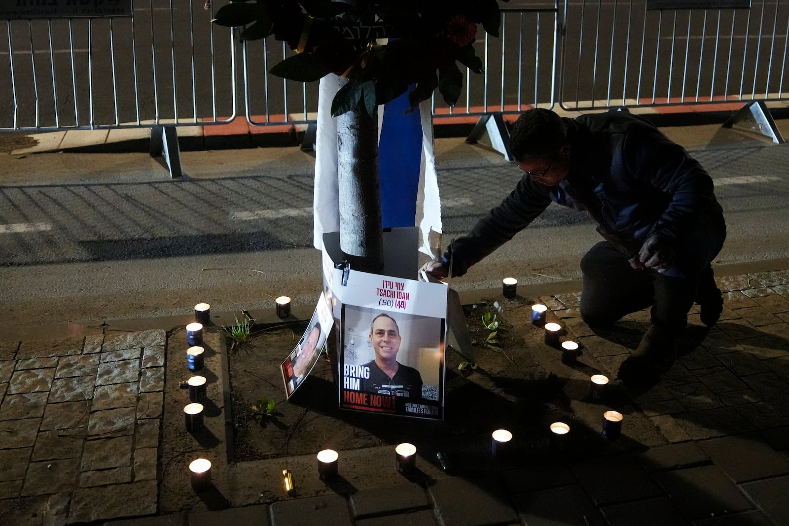 A man lights candles and displays photos of what Hamas says are four dead Israeli hostages handed over to Israel, outside the Abu Kabir Forensic Institute in Tel Aviv, Israel, while awaiting their arrival and identification on Thursday, Feb. 27, 2025. (AP Photo/Mahmoud Illean)