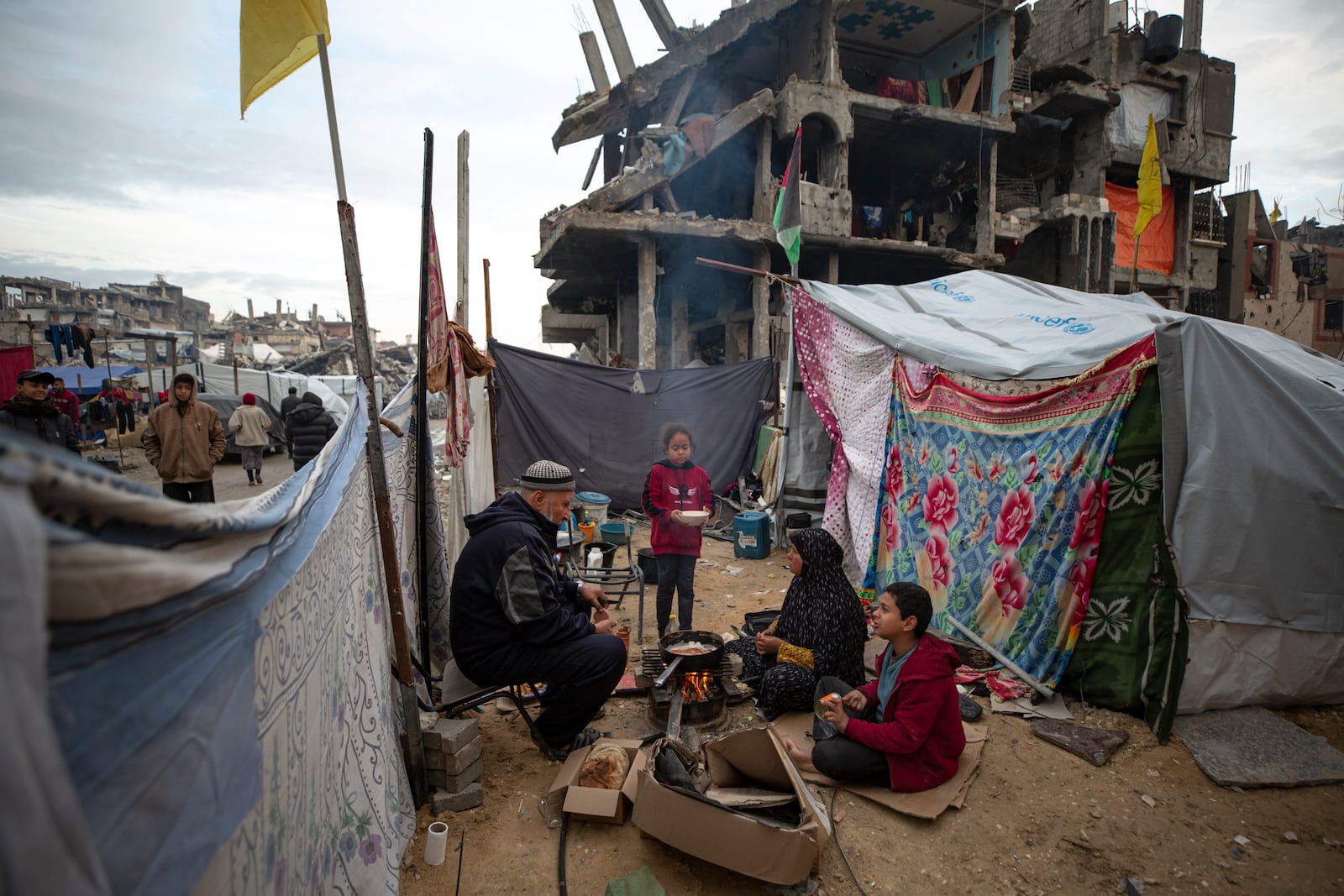 A Palestinian family cooks on fire next to their tent, in an area largely destroyed by the Israeli army's air and ground offensive in Jabaliya, Gaza Strip, on Tuesday, Feb. 11, 2025. (AP Photo/Jehad Alshrafi)