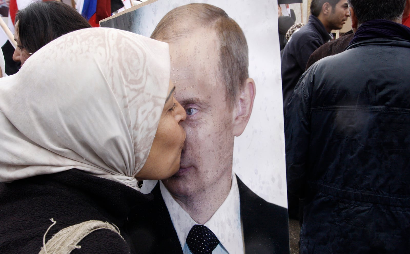 FILE - A Syrian woman kisses a poster of Russian President Vladimir Putin during a pro-government protest at the Russian Embassy in Damascus, Syria on March 4, 2012. (AP Photo/Muzaffar Salman, File)