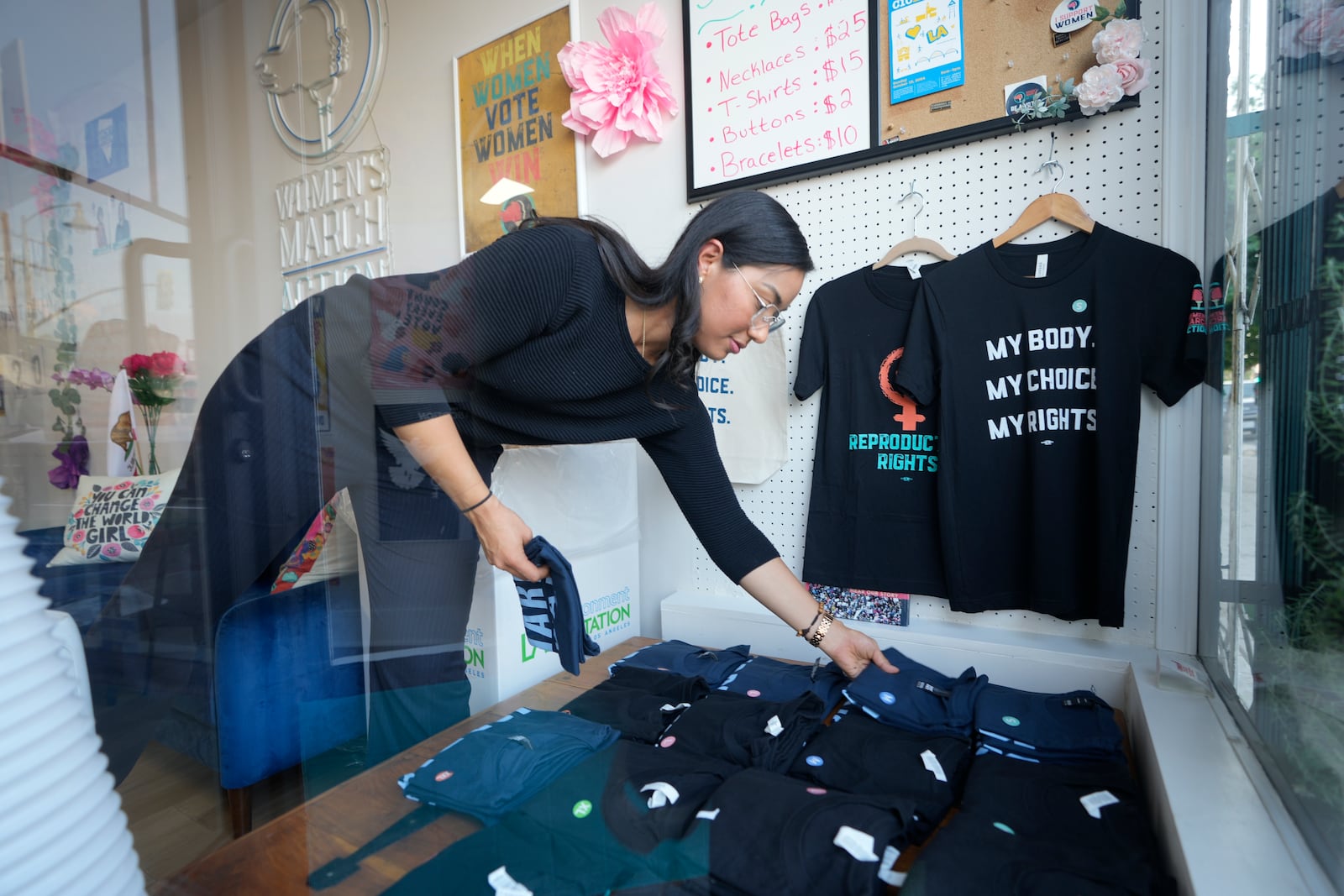 Advocate and volunteer Ivette Aragon adjusts T-shirts in the window of a phone bank where volunteers are calling voters to encourage them to vote for Democratic presidential nominee Vice President Kamala Harris in Los Angeles on Tuesday, Oct. 15, 2024. (AP Photo/Damian Dovarganes)