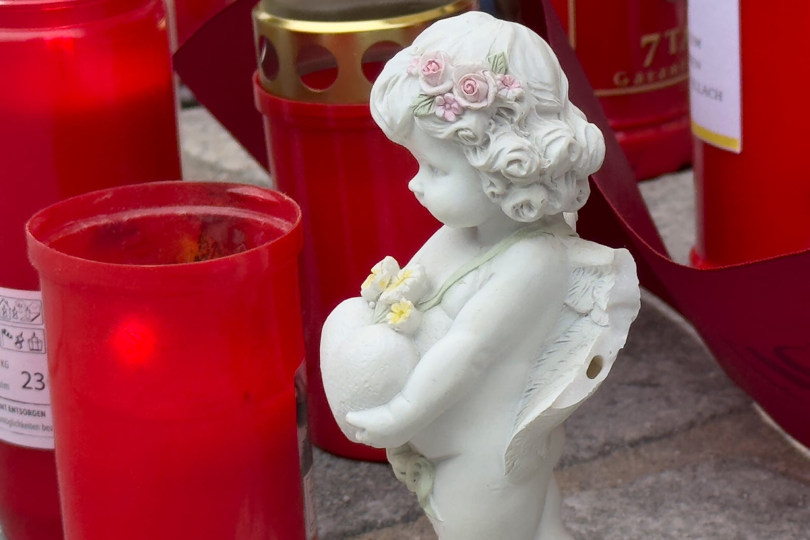 A figurine of angel is placed with candles at the site of stabbing a day after an attack that left a 14-year-old dead and five others injured, in Villach, Austria, Sunday, Feb. 16, 2025. (AP Photo/Darko Bandic)