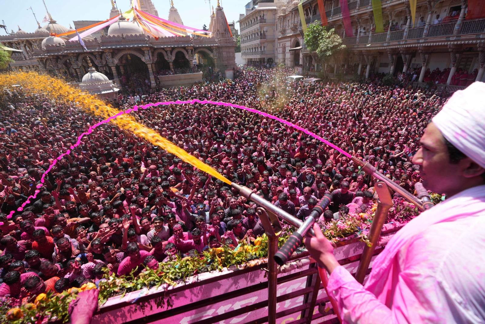 A priest sprays colored powder and water on devotees during celebrations of Holi, the Hindu festival of colors, at the Kalupur Swaminarayan temple in Ahmedabad, India, Friday, March 14, 2025. (AP Photo/Ajit Solanki)