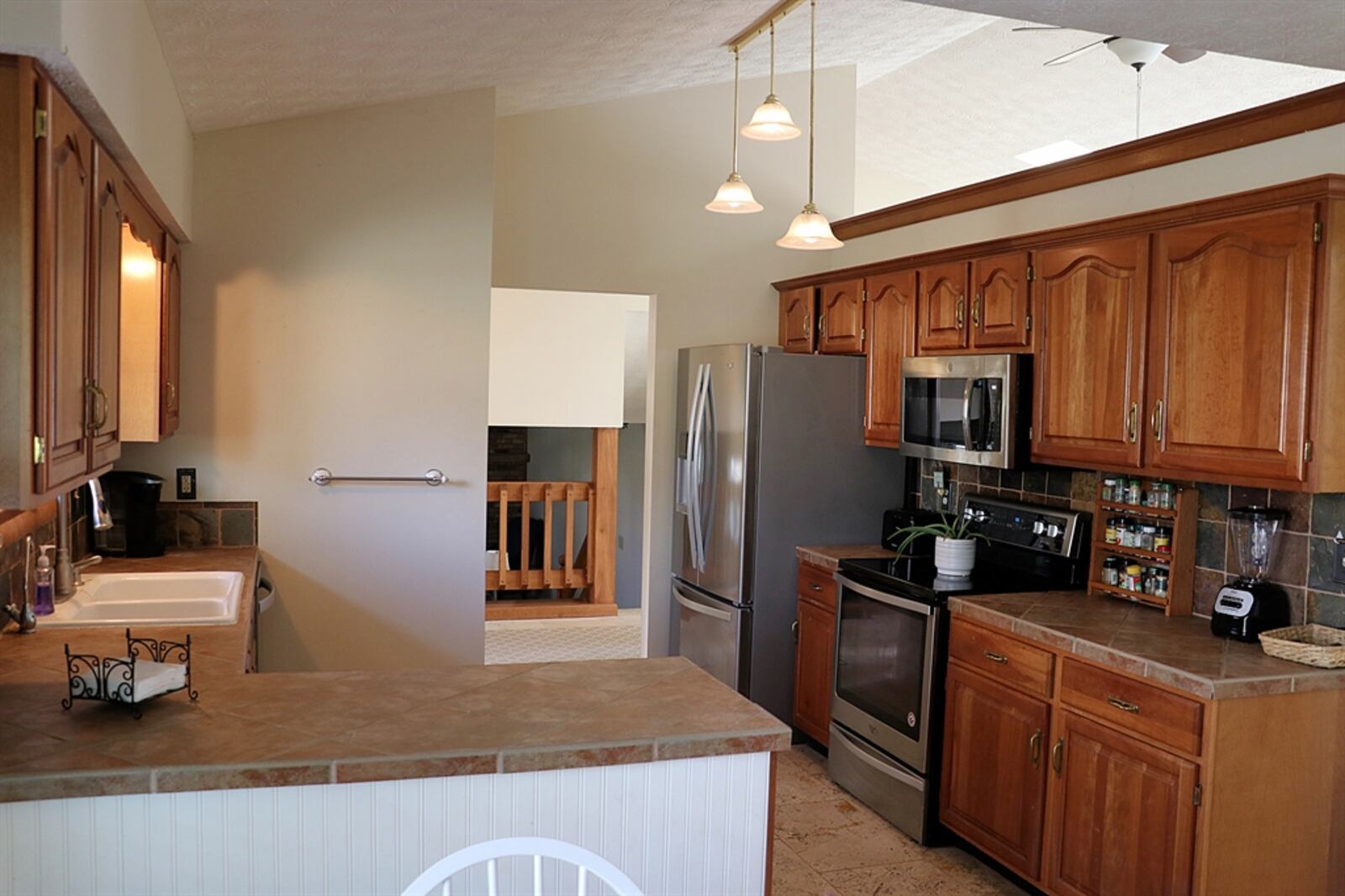 The kitchen and breakfast room are open to each other with a peninsula counter dividing the two spaces. A wood cap accents the wall space above the hanging cabinetry. 