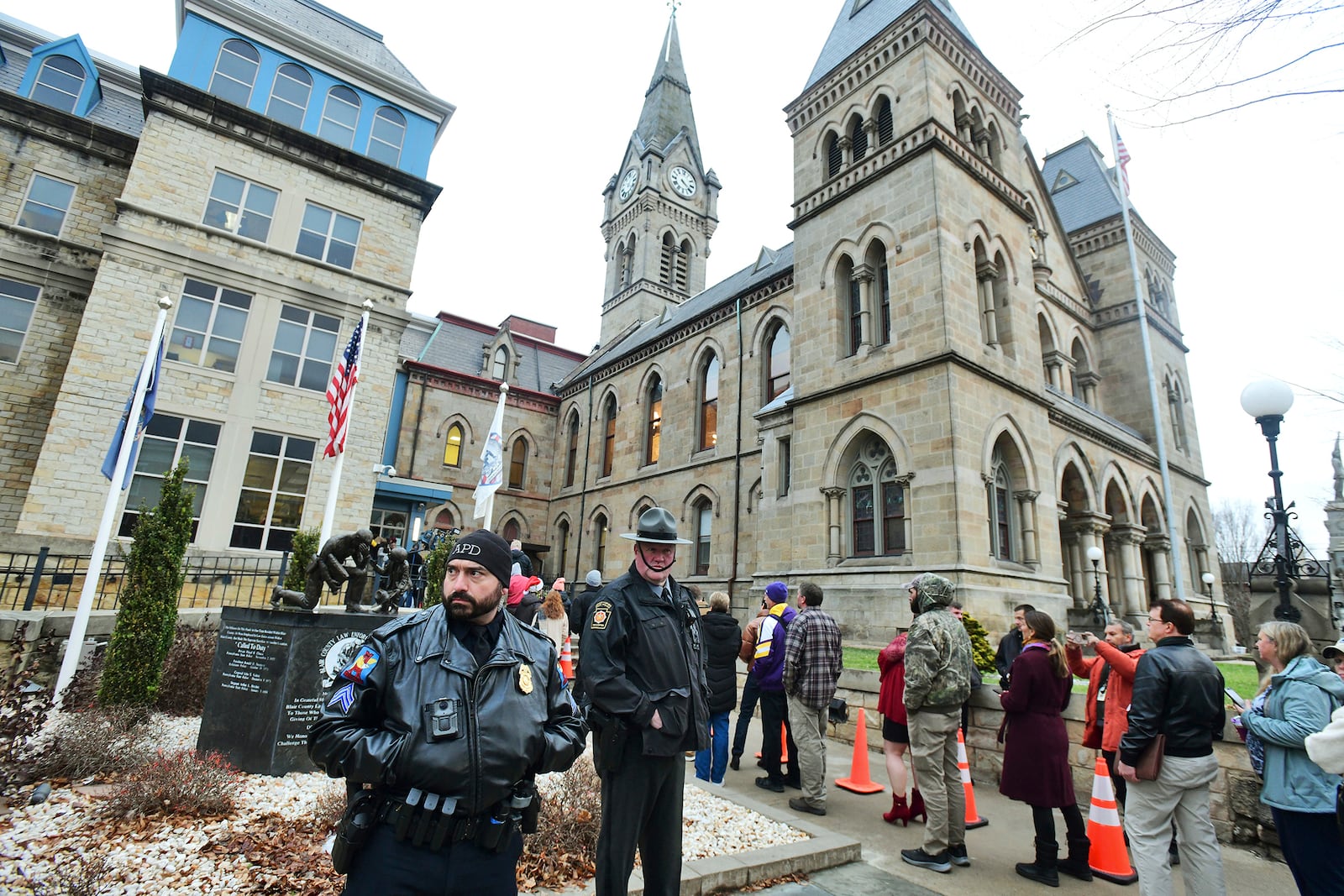 Pennsylvania State Police Troopers, Altoona Police Department and Hollidaysburg Police Department officers stand guard outside of the Blair County Courthouse as a line forms for the preliminary and extradition hearing for Luigi Nicholas Mangione in Hollidaysburg, Pa., Thursday, Dec. 19, 2024. (Thomas Slusser/The Tribune-Democrat via AP)