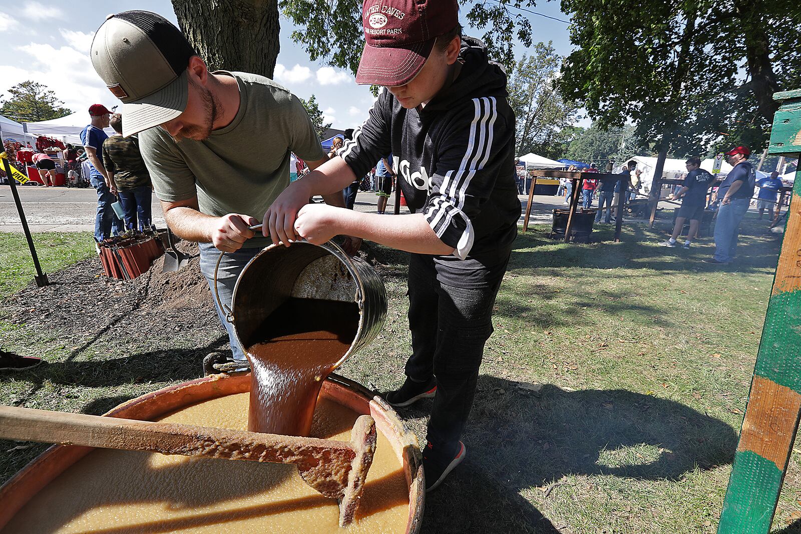 Jacob Juergens, left, and Caelek Stephany, both members of the Murphy family, pour the brown sugar mixture into one of the cauldrons of cooking apple butter at the Enon Apple Butter Festival. BILL LACKEY/STAFF 