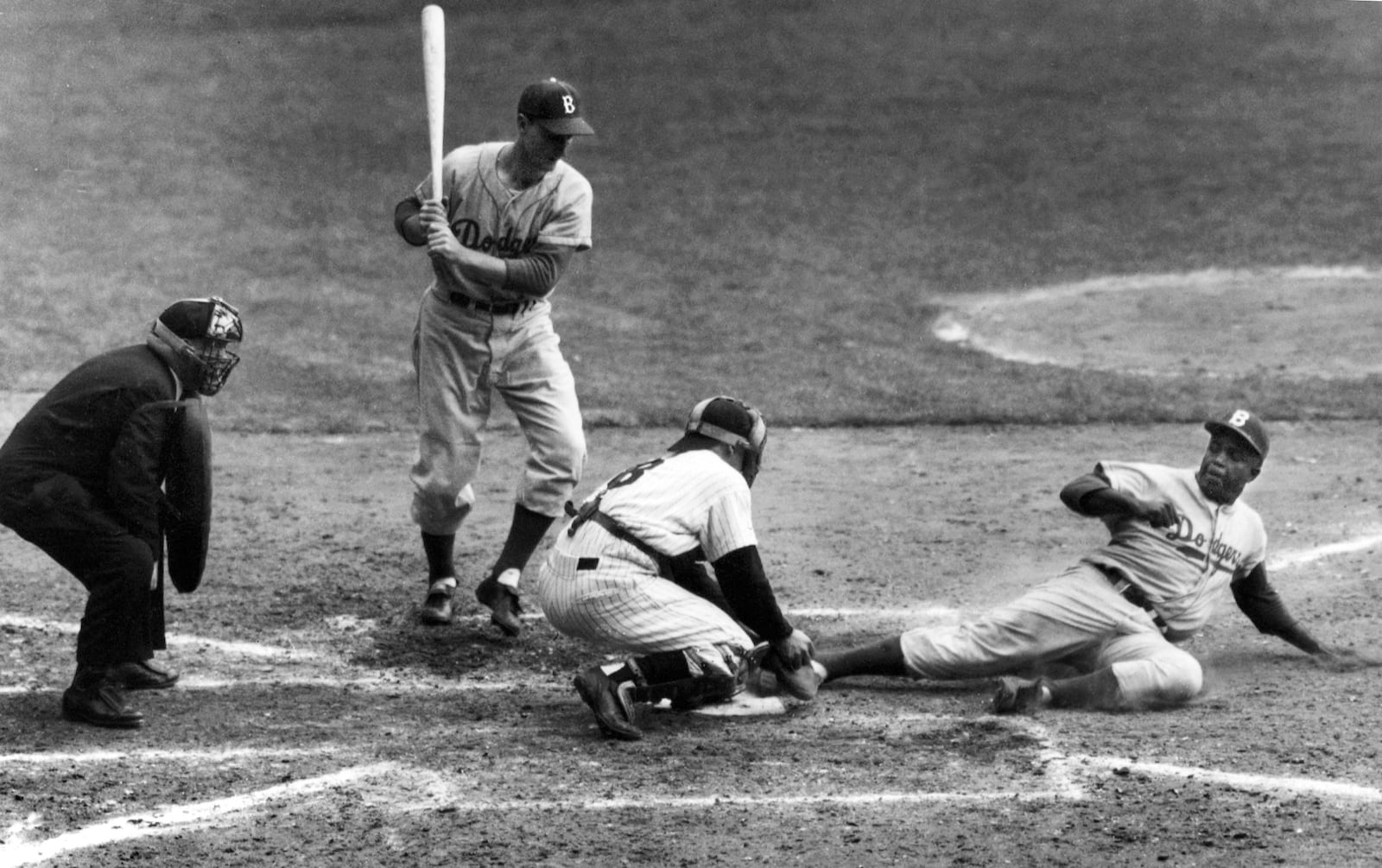 FILE - Brooklyn Dodgers' Jackie Robinson safely steals home plate under the tag of New York Yankees catcher Yogi Berra as pinch-hitter Frank Kellert looks on in the eighth inning of the World Series opener at New York's Yankee Stadium, Sept. 28, 1955. (AP Photo/John Rooney, File)