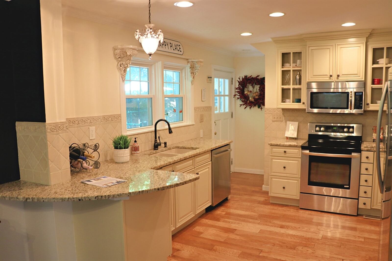 The kitchen has a pantry cabinet, and some hanging cabinets have glass-panel doors. Granite counters provide workspace, and the rounded peninsula offers breakfast bar seating. A window is above the double sink, and a door opens from the kitchen out to the fenced backyard.