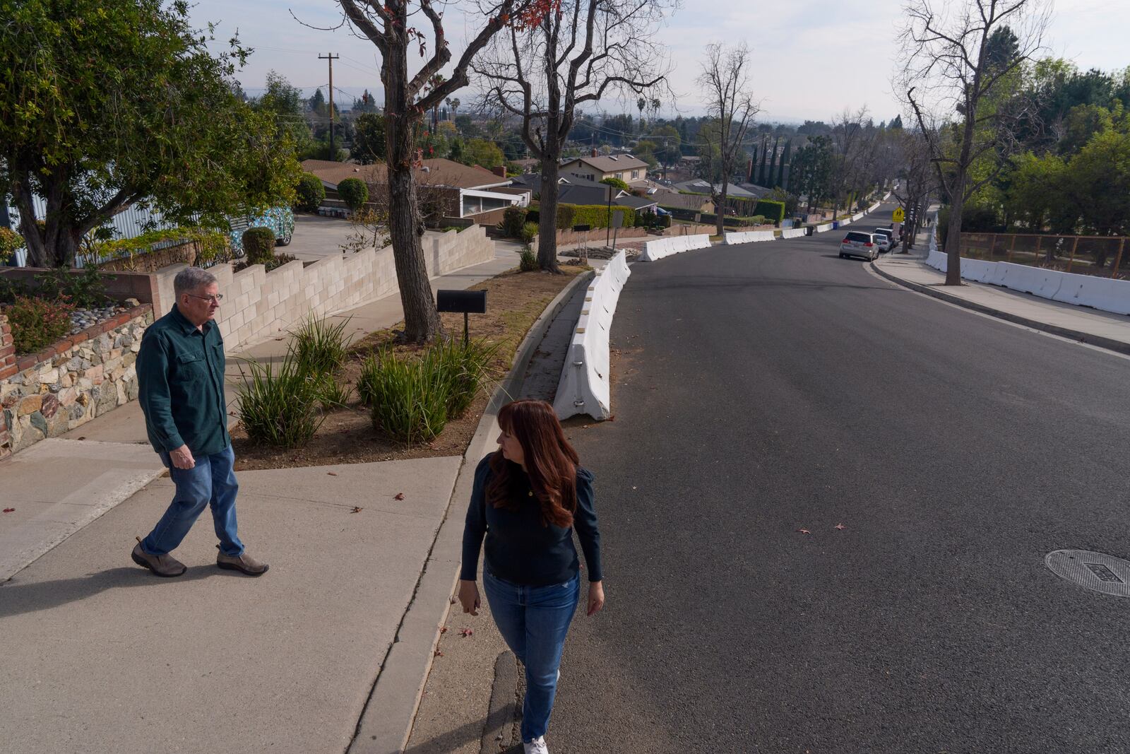 Duarte former Councilmember, John Fasana and resident Cici Carroll walk past concrete guard rails set in Duarte, Calif., Friday, Jan. 31, 2025, after wildfires. (AP Photo/Damian Dovarganes)