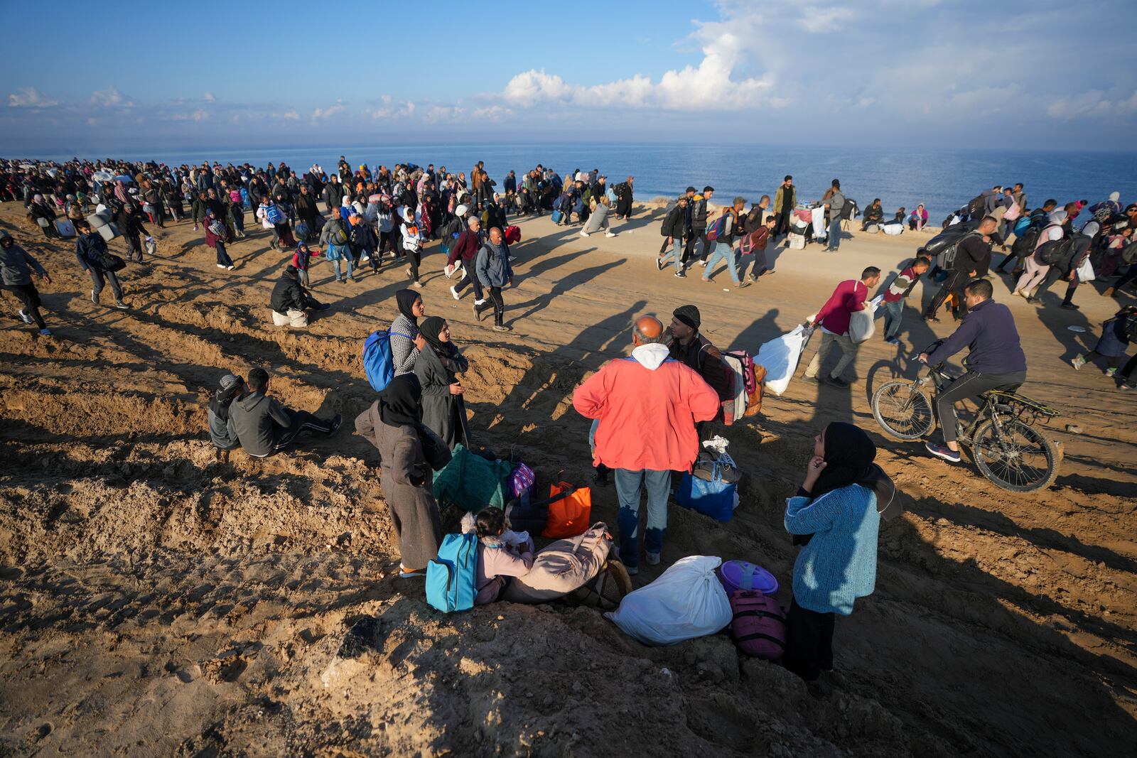 Ne'man Abu Jarad, in red jacket, and his family take a break as thousands of displaced Palestinians return to their homes in the northern Gaza Strip, following Israel's decision to allow them to go back for the first time since the early weeks of the 15-month war with Hamas, Monday, Jan. 27, 2025. (AP Photo/Abdel Kareem Hana)