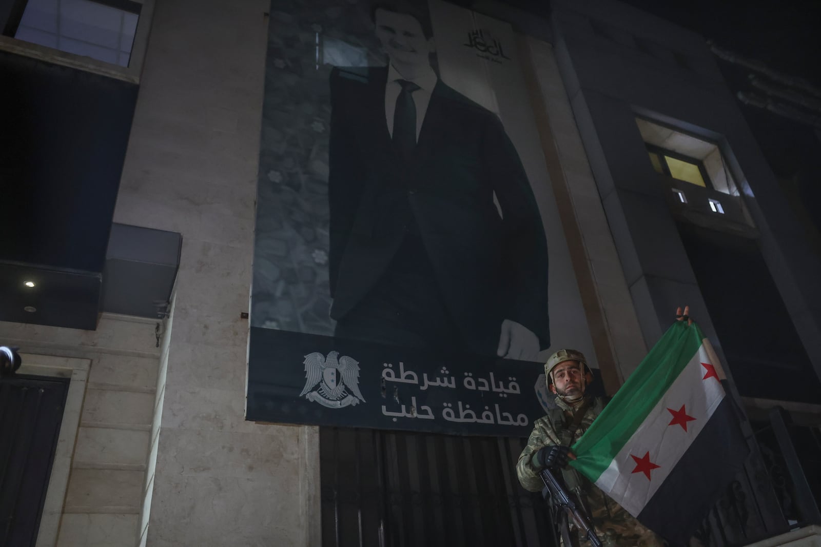 An opposition fighter poses with an opposition flag in front of a police station in Aleppo, Syria, late Friday, Nov. 29, 2024. (AP Photo/Ghaith Alsayed)