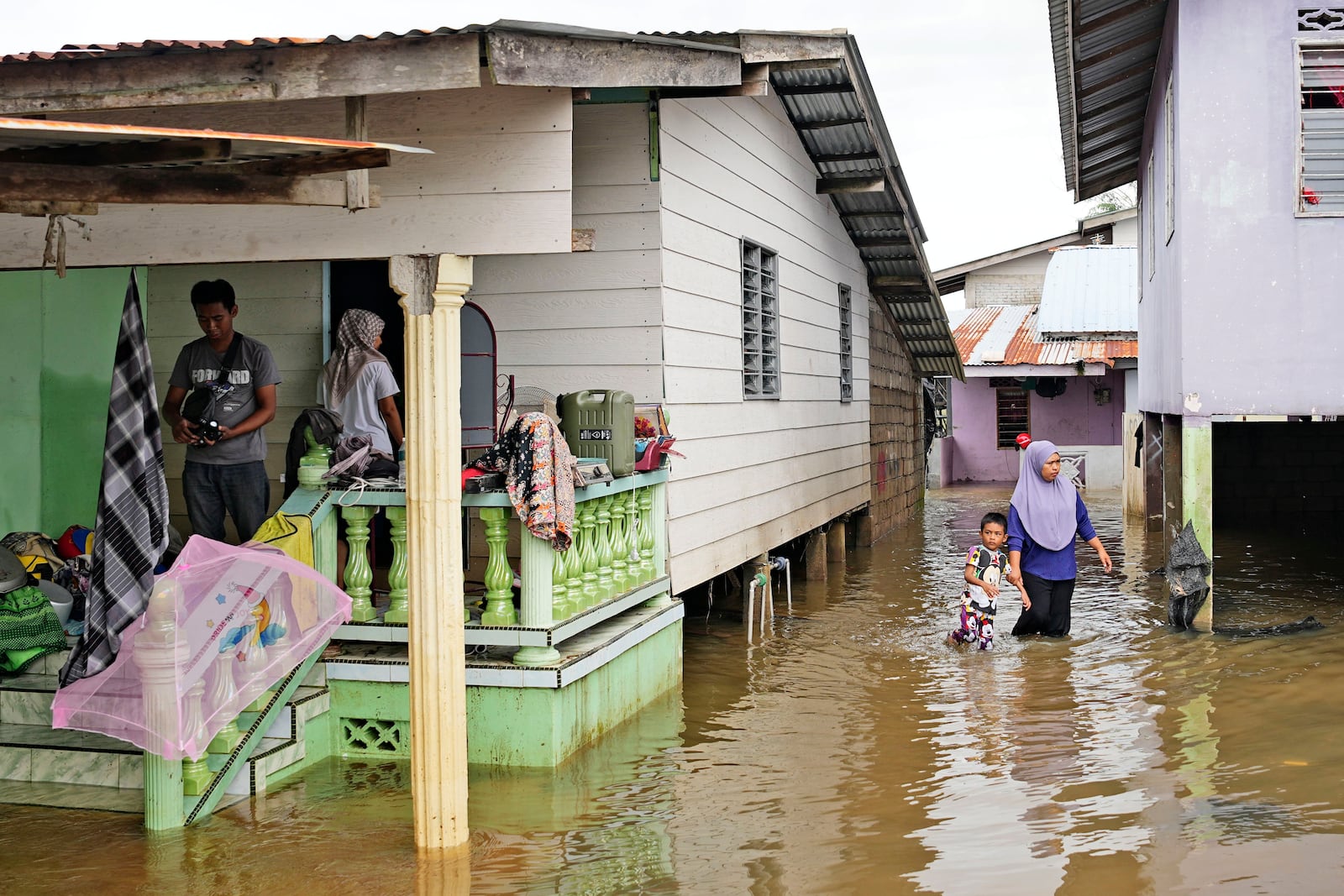 People wade through the water at a neighborhood affected by a flood in Tumpat, on the outskirts of Kota Bahru, Malaysia, Tuesday, Dec. 3, 2024. (AP Photo/Vincent Thian)