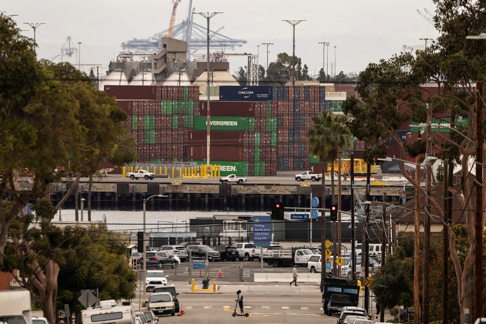 A person on a scooter crosses a street in a residential area located right next to the Port of Los Angeles, Tuesday, March 11, 2025, in San Pedro, Calif. (AP Photo/Etienne Laurent)