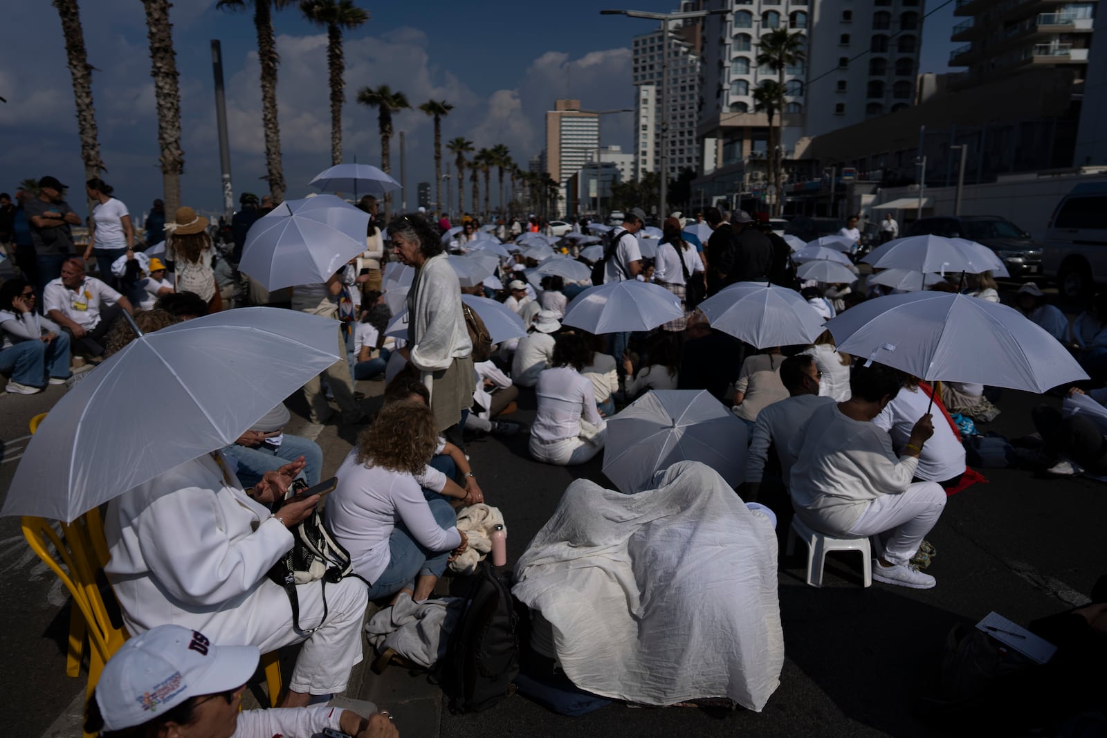 Activists sit on a road with white umbrellas during a protest calling for the release of hostages held in the Gaza Strip, in front of the U.S. Embassy branch office in Tel Aviv, Israel, Friday, Jan. 31, 2025. (AP Photo/Oded Balilty)