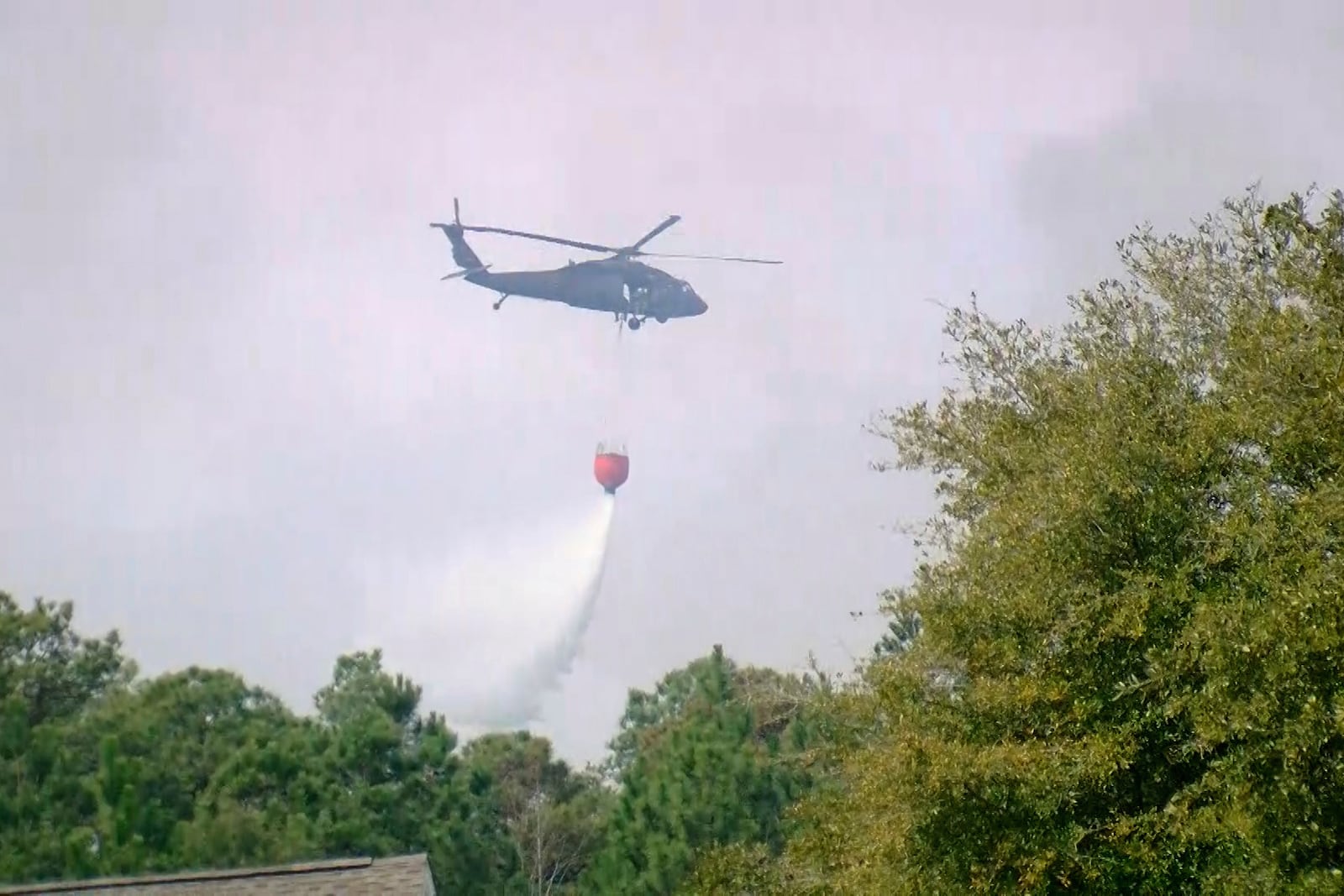 A helicopter drops water to help contain a fire in the Carolina Forest area west of the coastal resort city of Myrtle Beach, S.C., Sunday, March 2, 2025, where residents were ordered to evacuate several neighborhoods. (WMBF-TV via AP)