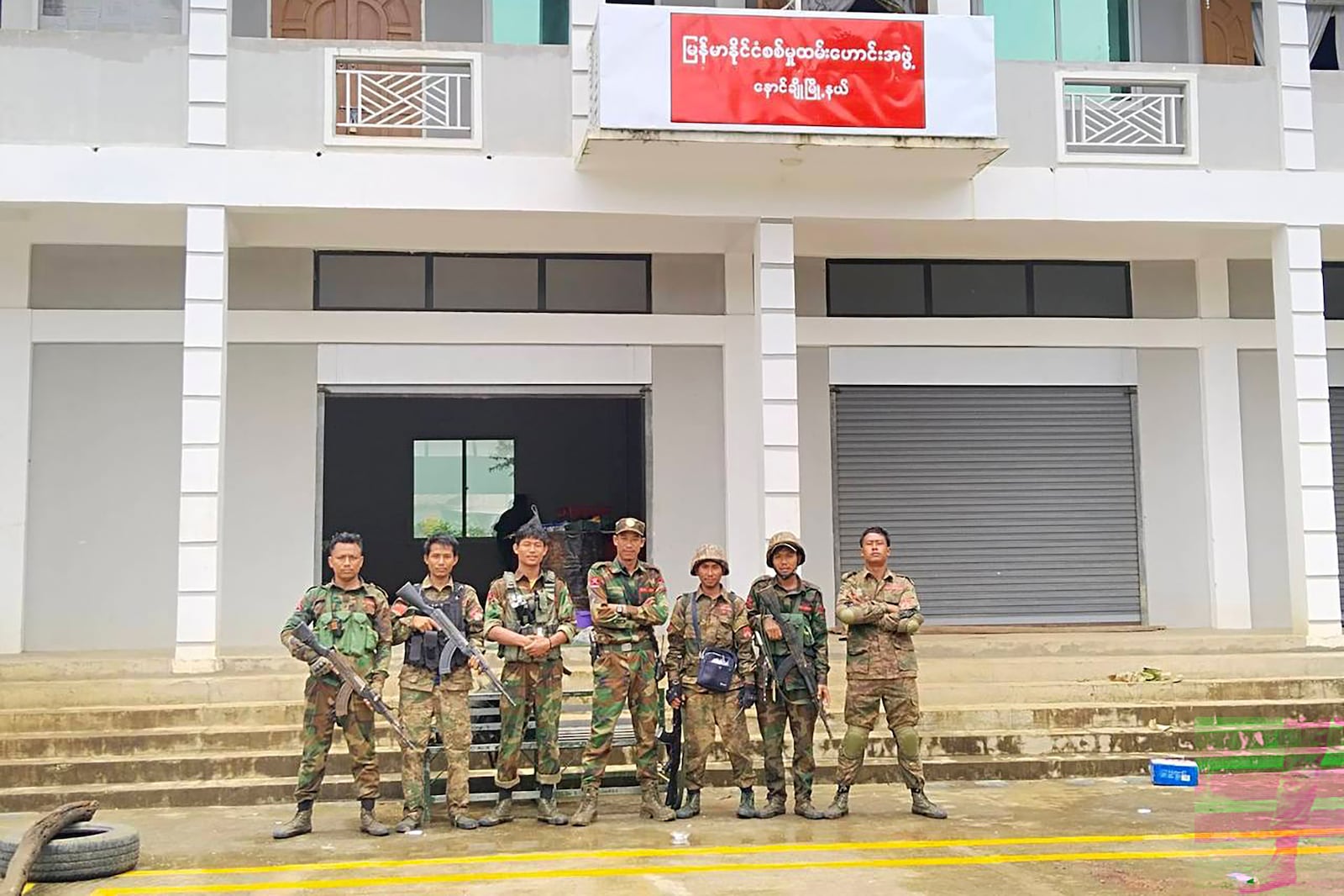 In this photo provided by Mandalay People's Defence, members of the Ta'ang National Liberation Army, one of the ethnic armed forces in the Brotherhood Alliance, and Mandalay People's Defence Force pose for a photograph in front of the captured building of the Myanmar's War Veterans' Organisation in Nawnghkio township in Shan state, Myanmar, on June 26, 2024. (Mandalay People's Defence Force via AP)