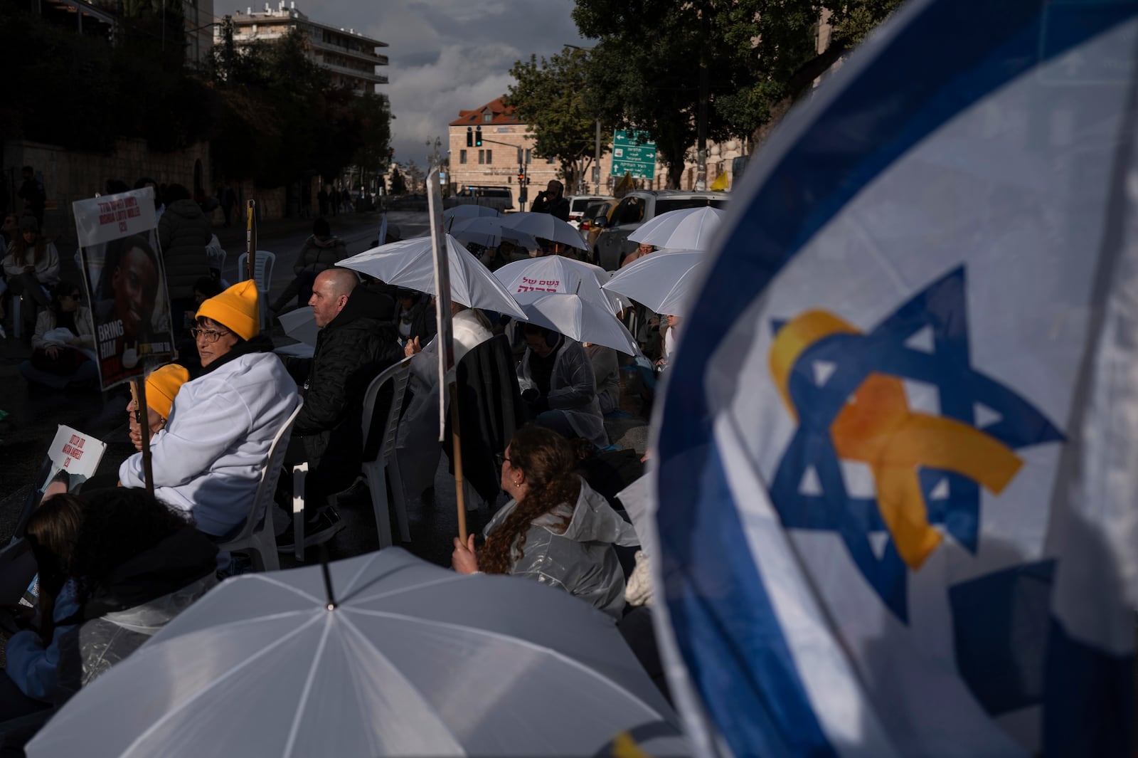 Activists sit on a road with white umbrellas during a protest calling for the release of hostages held in the Gaza Strip, outside the prime minister's house in Jerusalem, Wednesday, Feb. 12, 2025. (AP Photo/Ohad Zwigenberg)