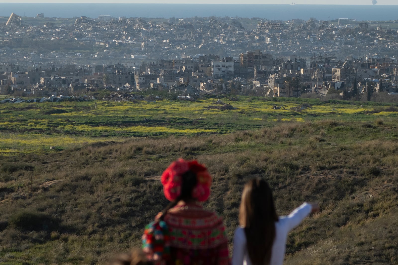 People look at buildings that were destroyed during the Israeli air and ground offensive stand in the Gaza Strip as seen from southern Israel, Sunday, March 2, 2025. (AP Photo/Leo Correa)