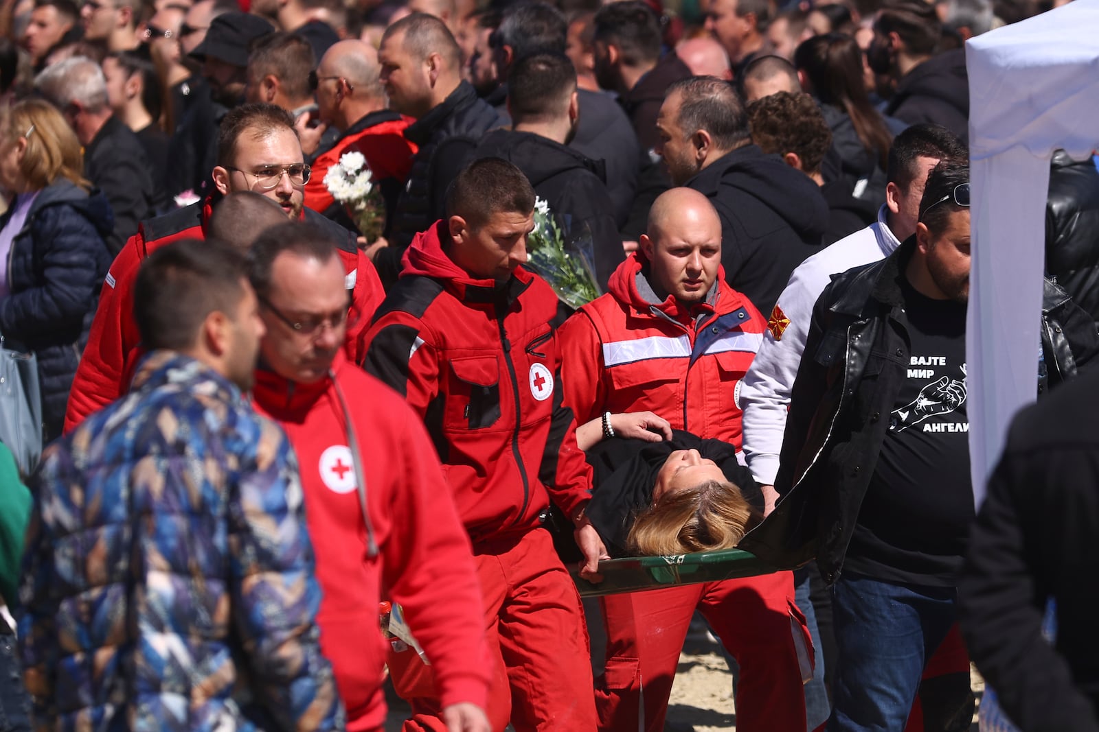 Paramedics carry a woman who collapsed during the funeral ceremony of the victims of a massive nightclub fire in the town of Kocani, North Macedonia, Thursday, March 20, 2025. (AP Photo/Armin Durgut)