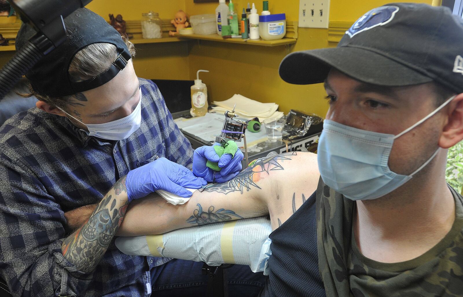 Robert Lamb, of Truth and Triumph Tattoo, works on the tattoo of Tyler Milligan. Companies are allowed to reopen if they follow state rules for health and safety, including requiring employees to wear face masks. MARSHALL GORBYSTAFF