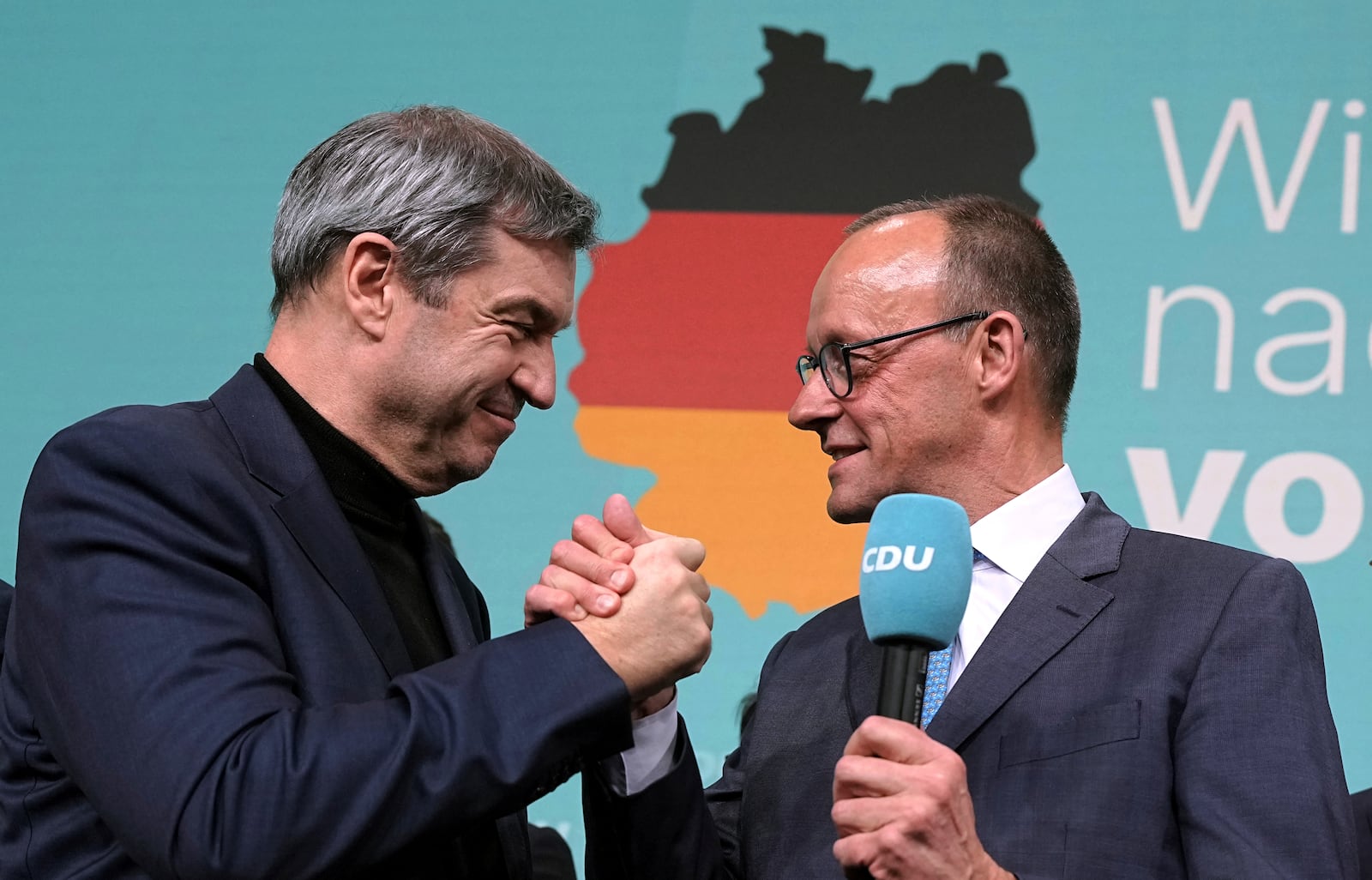 Friedrich Merz, right, leader of the Christian Democratic Union (CDU), and Markus Soeder, leader of the Christian Social Union (CSU), shake hands at the CDU party headquarters in Berlin, Germany, Sunday, Feb. 23, 2025. (Michael Kappeler/dpa via AP)