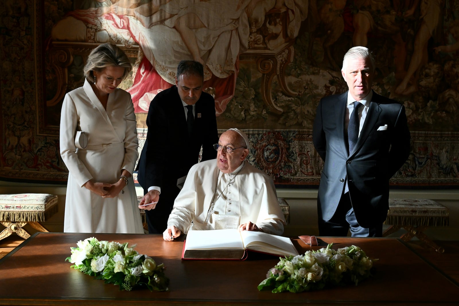 Pope Francis, center, signs the book of honor during his visit to King Philippe of Belgium, right, and Queen Mathilde at the Castle of Laeken, Belgium, Friday, Sept. 26, 2024, on the second day of a four-day apostolic journey to Luxembourg and Belgium. (Alberto Pizzoli/pool photo via AP)