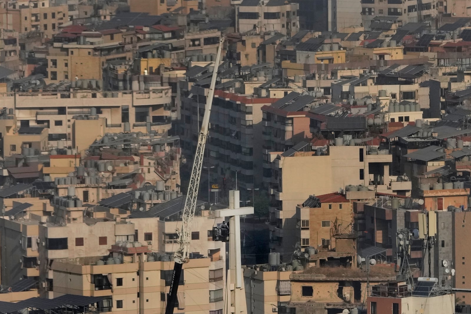 Workers in a crane basket, fix the giant cross of Our Lady of Hadath Church, with Dahiyeh, the southern suburb of Beirut seen in the background, Lebanon, Friday, Nov. 1, 2024. (AP Photo/Hussein Malla)