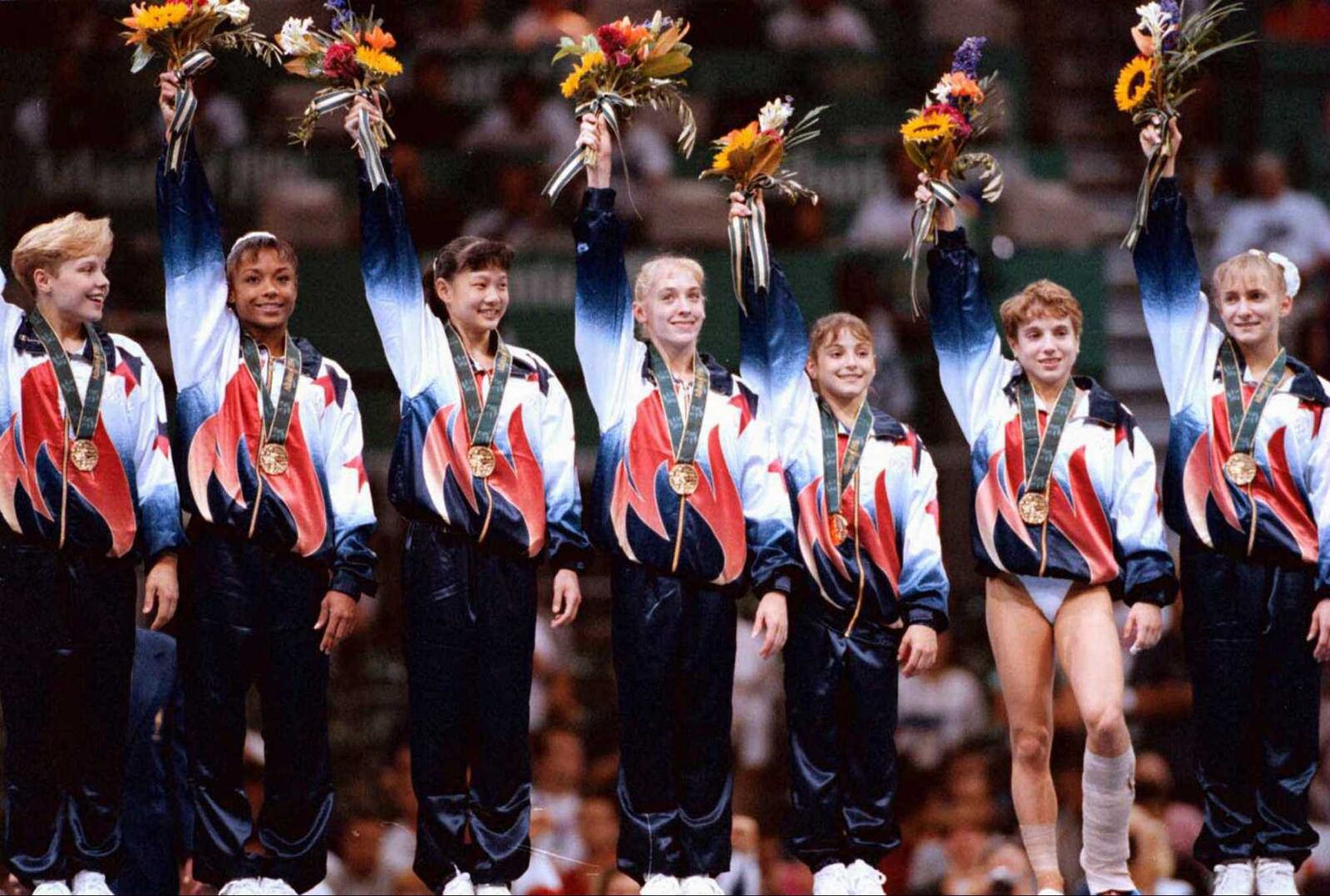 The U.S. women's team -- with Strug gamely standing on her bandaged leg -- accepts their gold medal in the team competition to the cheers of the home country crowd in the Georgia Dome. AJC file photo