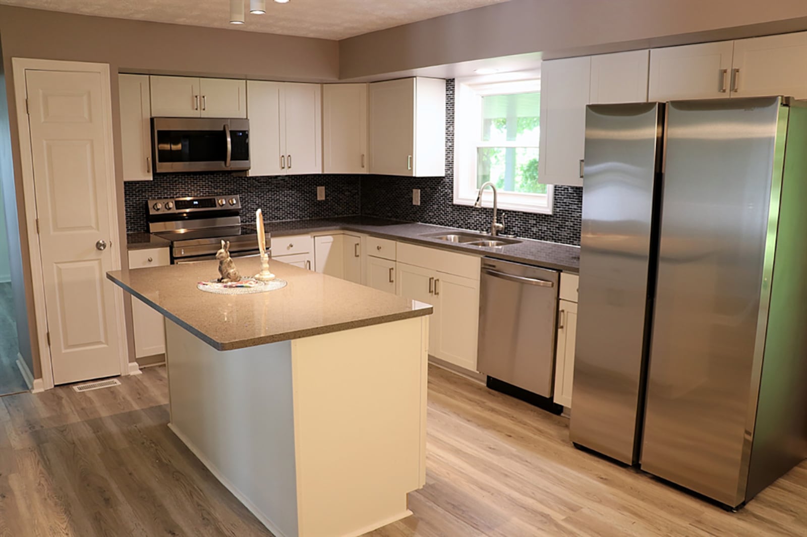 Mosaic-glass tile accents the wall space and gives a little color to the totally renovated white and gray kitchen. White cabinetry fills two walls and surrounds stainless-steel appliances that include a range, dishwasher, microwave and refrigerator. An island offers bar seating for two and has additional storage. CONTRIBUTED PHOTO BY KATHY TYLER