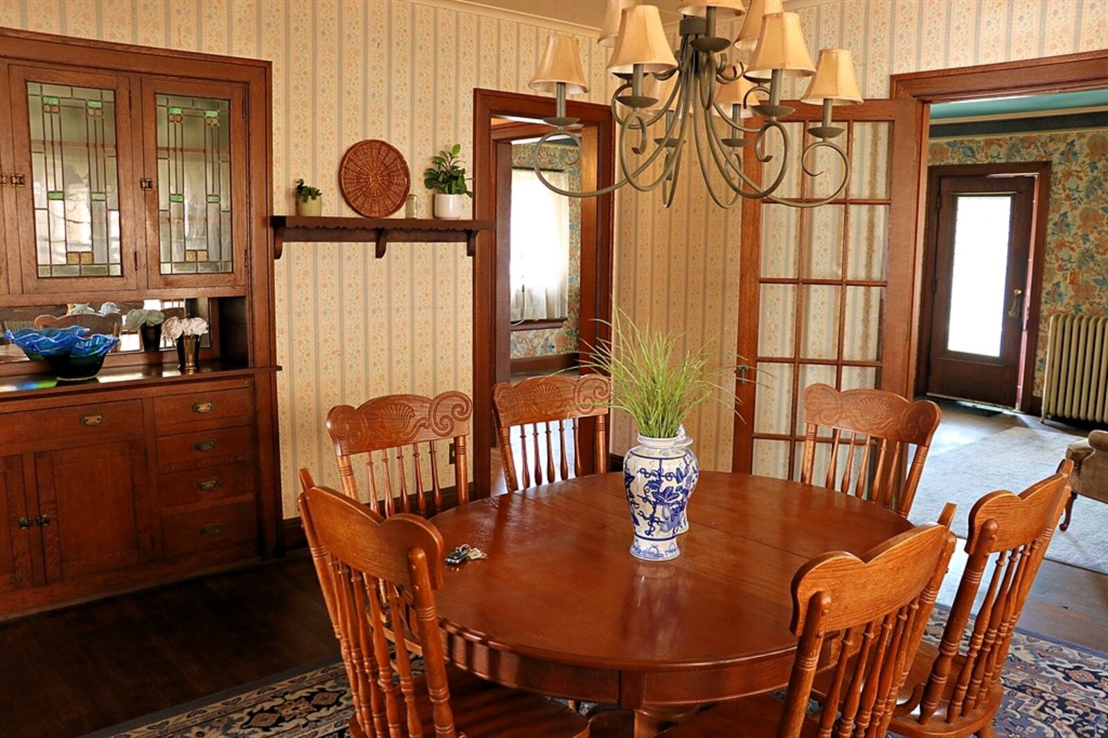 French doors open into a formal dining room that has a wall of windows on one side and a built-in buffet cabinet within the other wall. 