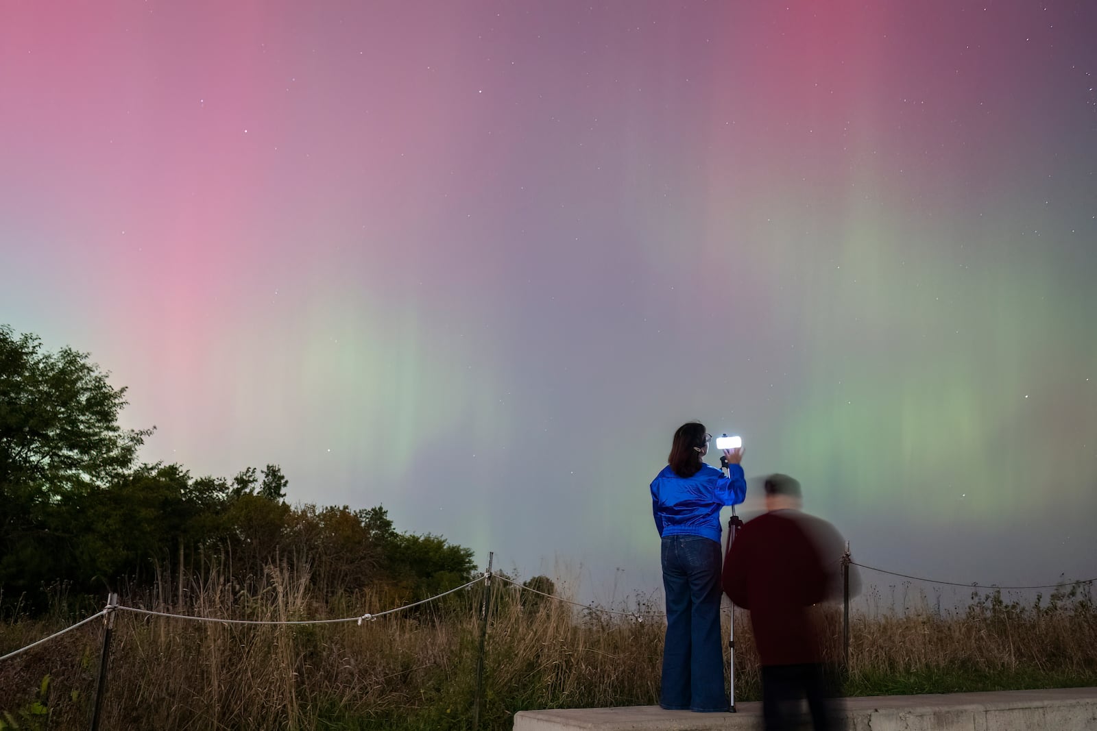 People watch as an aurora borealis, also known as the northern lights, lights up the night sky from Montrose Point, Thursday, Oct. 10, 2024, in Chicago. (Tyler Pasciak LaRiviere/Chicago Sun-Times via AP)