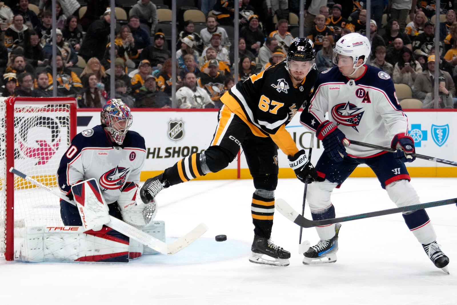 Pittsburgh Penguins' Rickard Rakell (67) gets out of the way of a shot in front of Columbus Blue Jackets goaltender Elvis Merzlikins (90) with Zach Werenski (8) defending during the second period of an NHL hockey game in Pittsburgh, Tuesday, Jan. 7, 2025. (AP Photo/Gene J. Puskar)