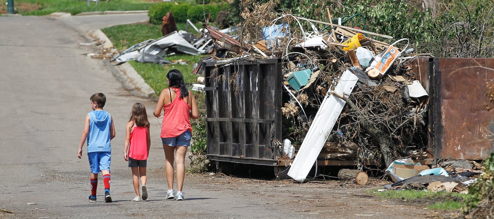 Sara Rice of Harrison Twp. and her children Brayden, 9, and Josie, 7, walk in front of a roll-off container placed near their home on Swallow Drive to collect building material debris. Officials ask that tree debris be left at the curb and not placed in the containers. CHRIS STEWART / STAFF