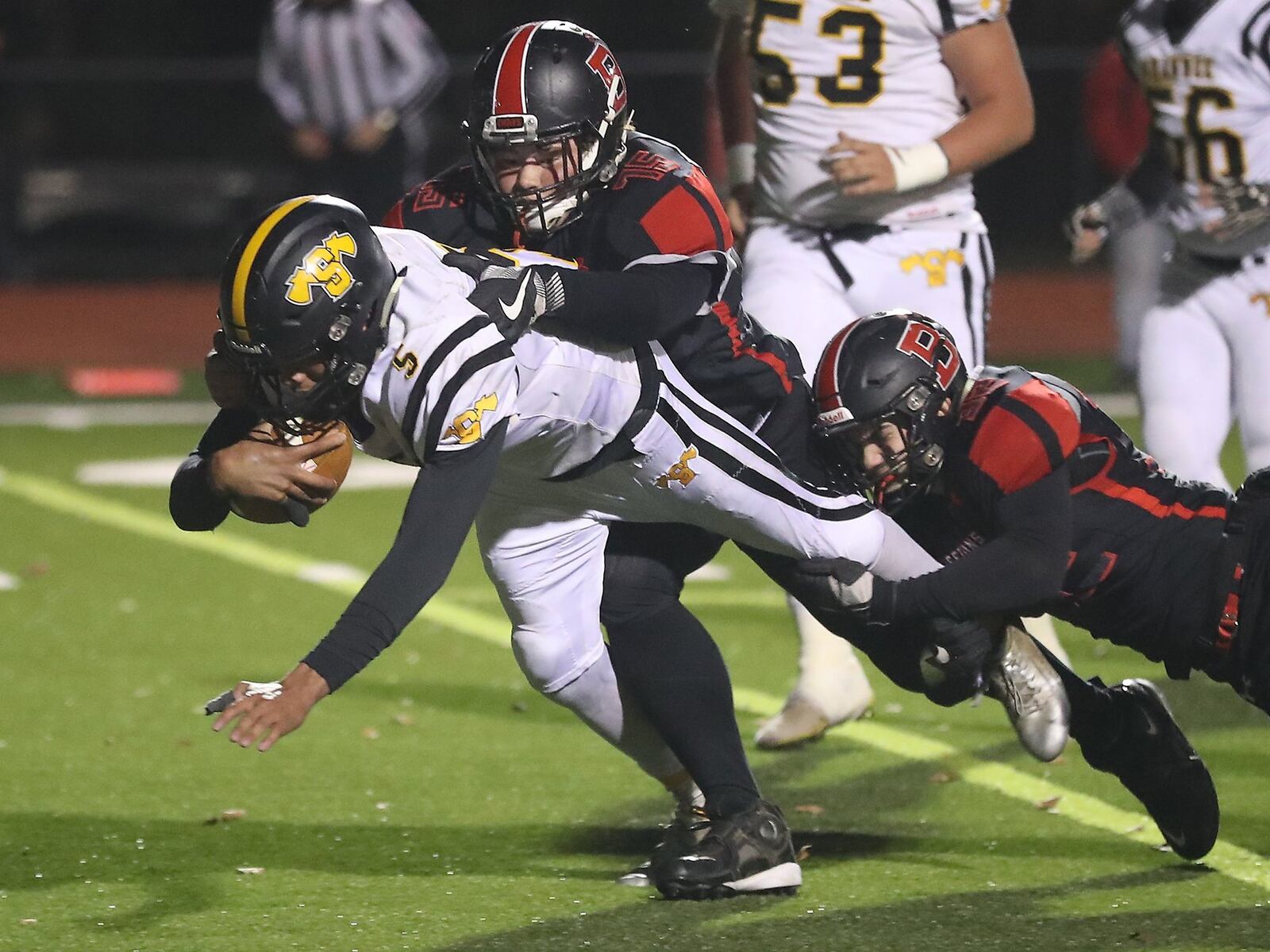 Shawnee’s Robie Glass dives for extra yards as he’s tackled by Bellefontaine’s Ryan Pool and DJ McDonald. BILL LACKEY/STAFF