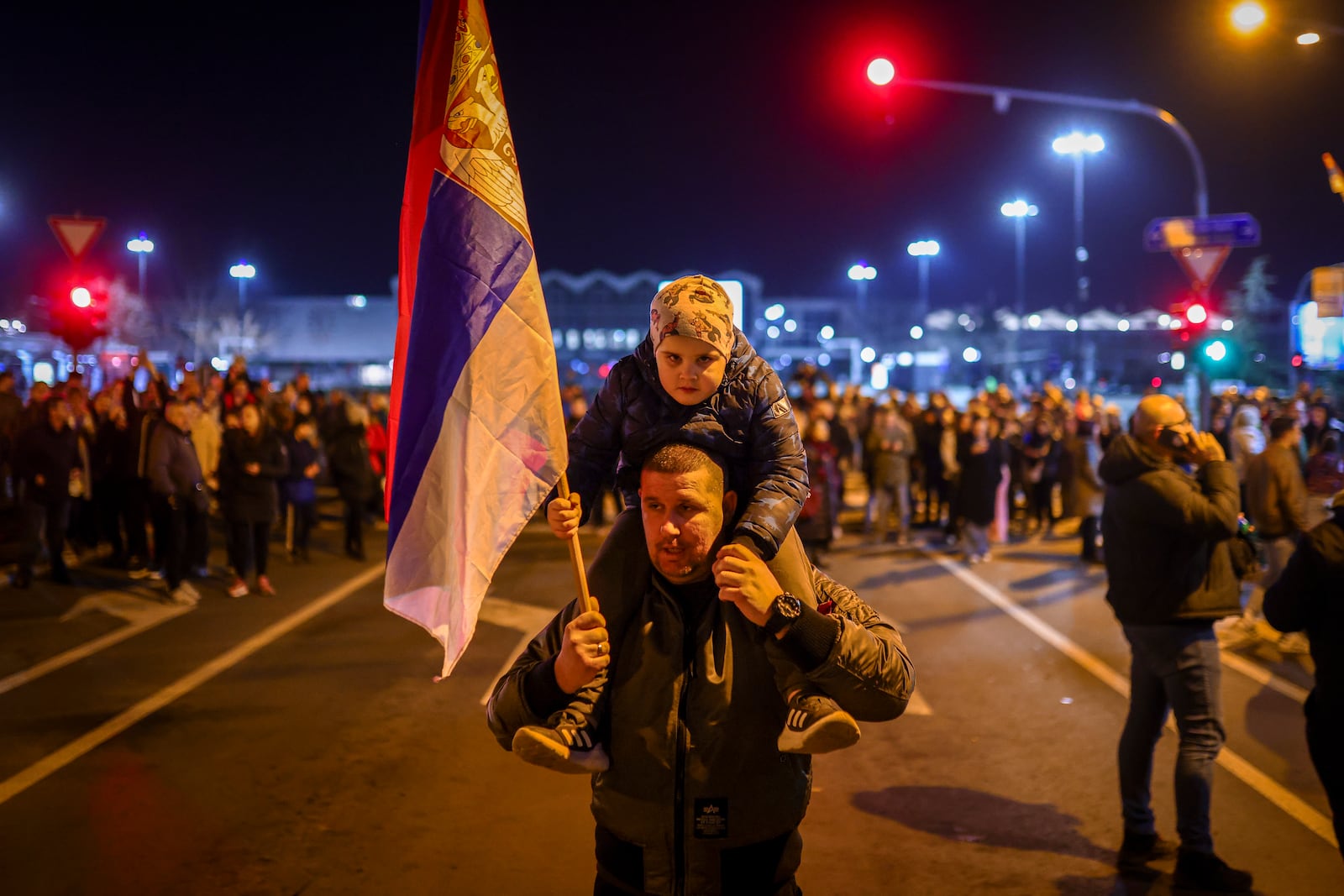 A man carrying a child on his shoulders holds the Serbian flag during a protest over the collapse of a concrete canopy that killed 15 people more than two months ago, in Novi Sad, Serbia, Friday, Jan. 31, 2025. (AP Photo/Armin Durgut)