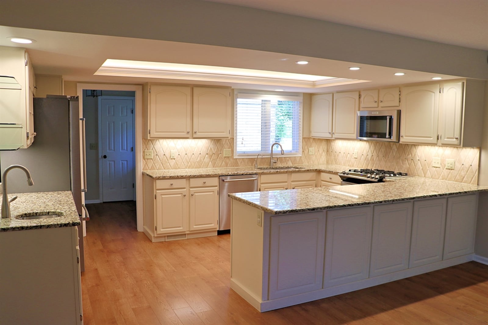 The U-shaped kitchen has a tray ceiling with extra canister lighting and granite counters on off-white cabinetry.