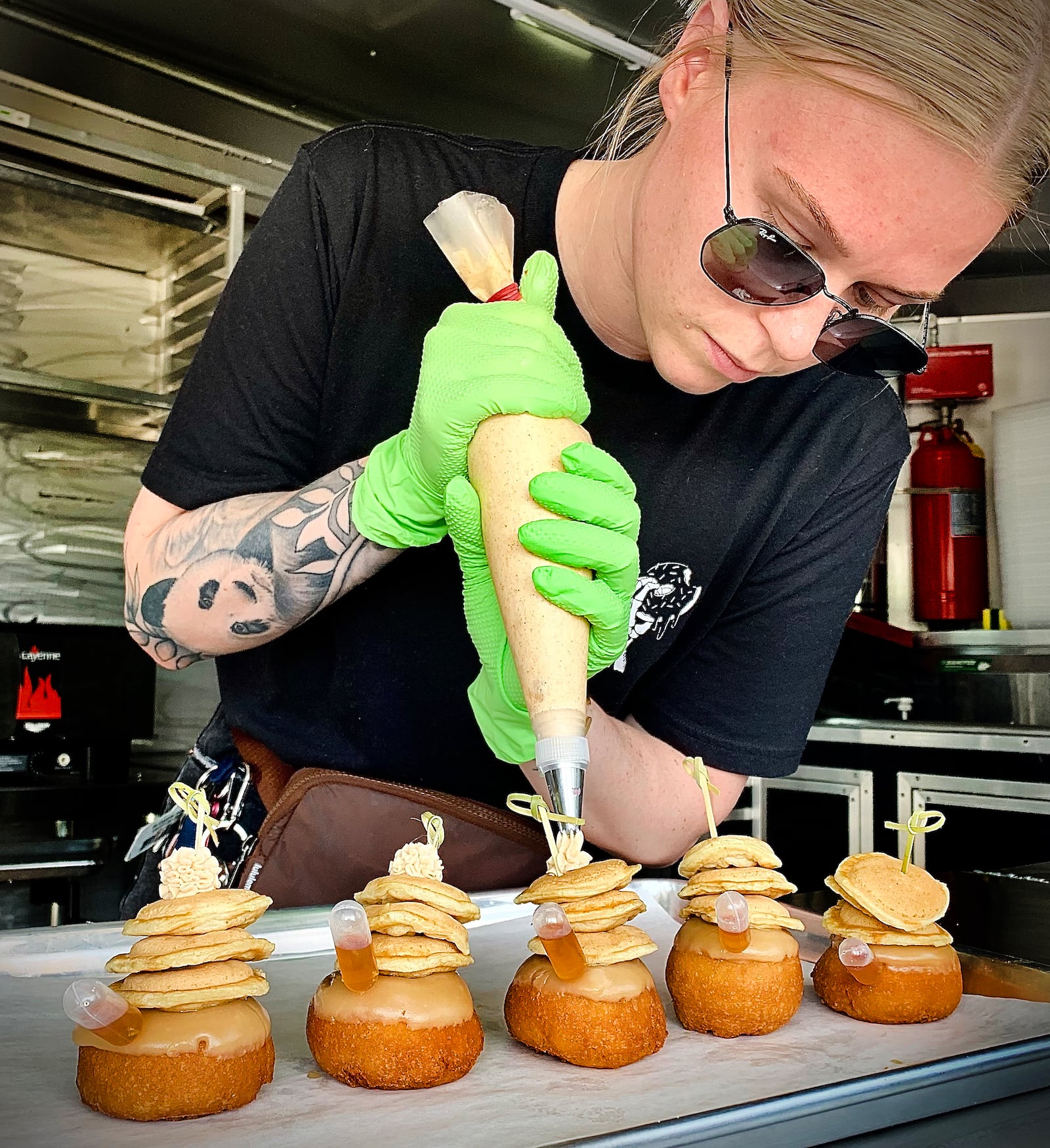 Death Grip Donuts is collaborating with Uncle Boof’s World Famous Pancake Mix for a “Locals Only” donut featuring a traditional vanilla donut with maple glaze, three mini pancakes and a dollop of cinnamon butter that’s served with a pipette of maple syrup. Pictured is Kylie Bauer adding cinnamon butter to the donuts. MARSHALL GORBY\STAFF