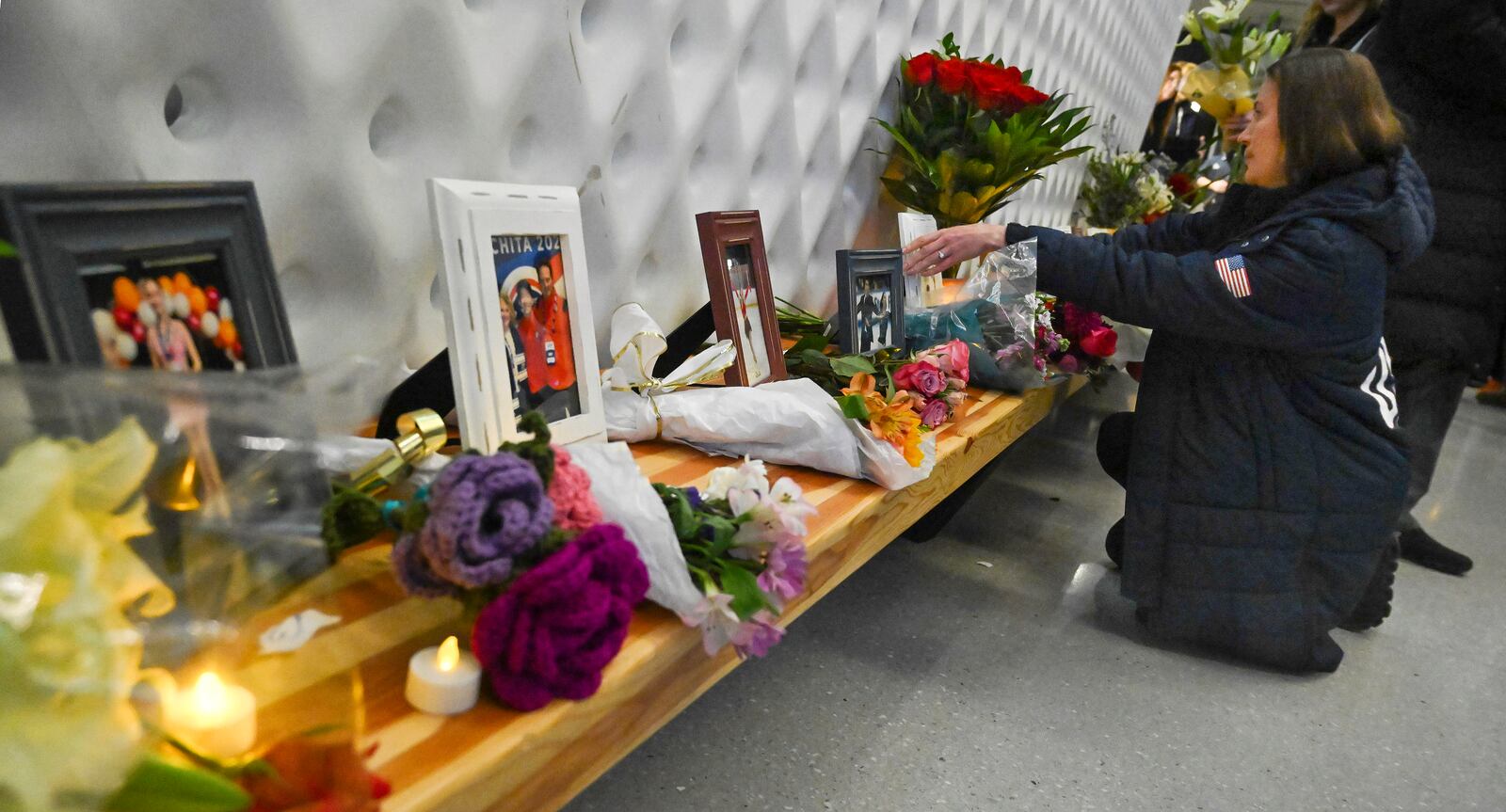 Ice dancing coach Elena Dostatni places flowers at a memorial of photos for the 28 skaters, family members and coaches who died in last week's plane crash in Washington, D.C. during a vigil held at the U.S. Olympic and Paralympic Museum in Colorado Springs, Colo., Monday, Feb. 3, 2025. (Jerilee Bennett/The Gazette via AP)