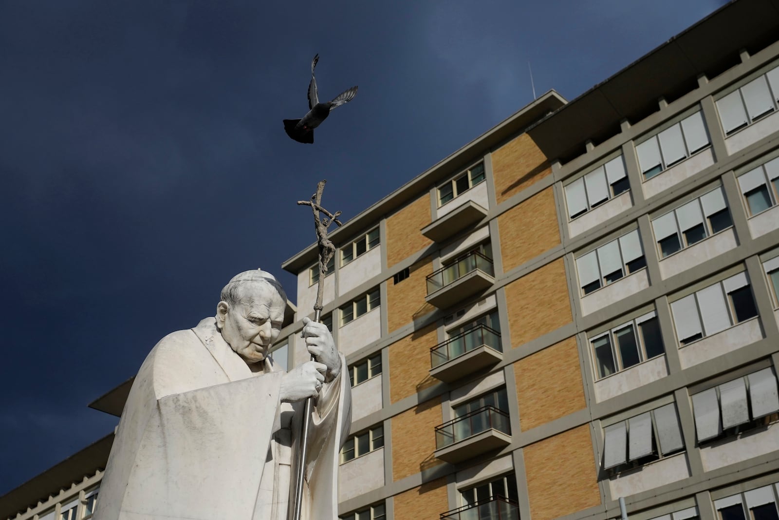 A marble statue of late Pope John Paul II is backdropped by the Agostino Gemelli Polyclinic in Rome, Saturday, Feb. 15, 2025, where Pope Francis was hospitalized Friday, Feb. 14, after a weeklong bout of bronchitis worsened and is receiving drug therapy for a respiratory tract infection. (AP Photo/Alessandra Tarantino)