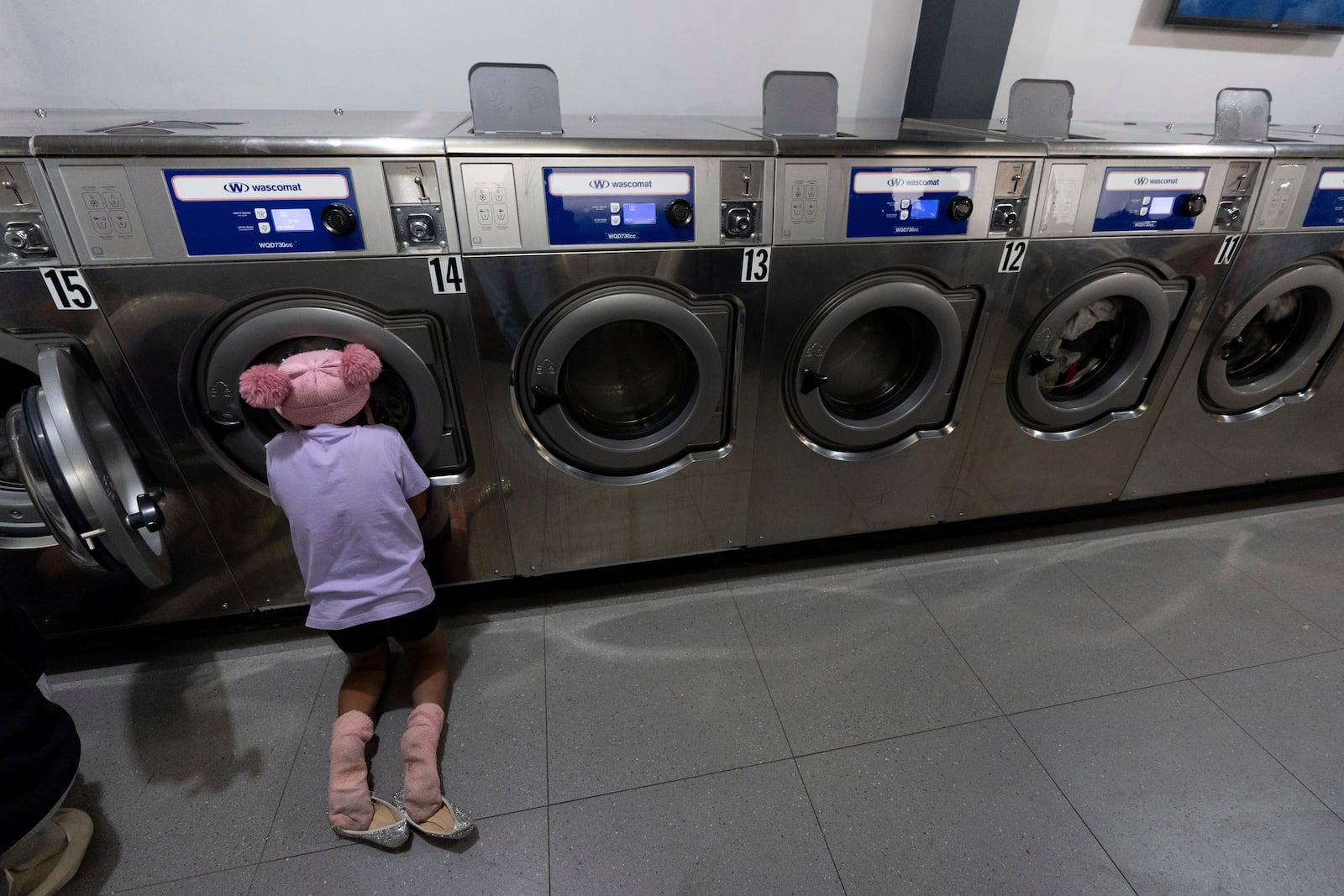 Maickeliys Rodriguez, 6, of Venezuela, watches her family's laundry spins in a machine at a laundromat near the migrant shelter where they are staying in Tijuana, Mexico, Friday, Jan. 31, 2025. (AP Photo/Gregory Bull)