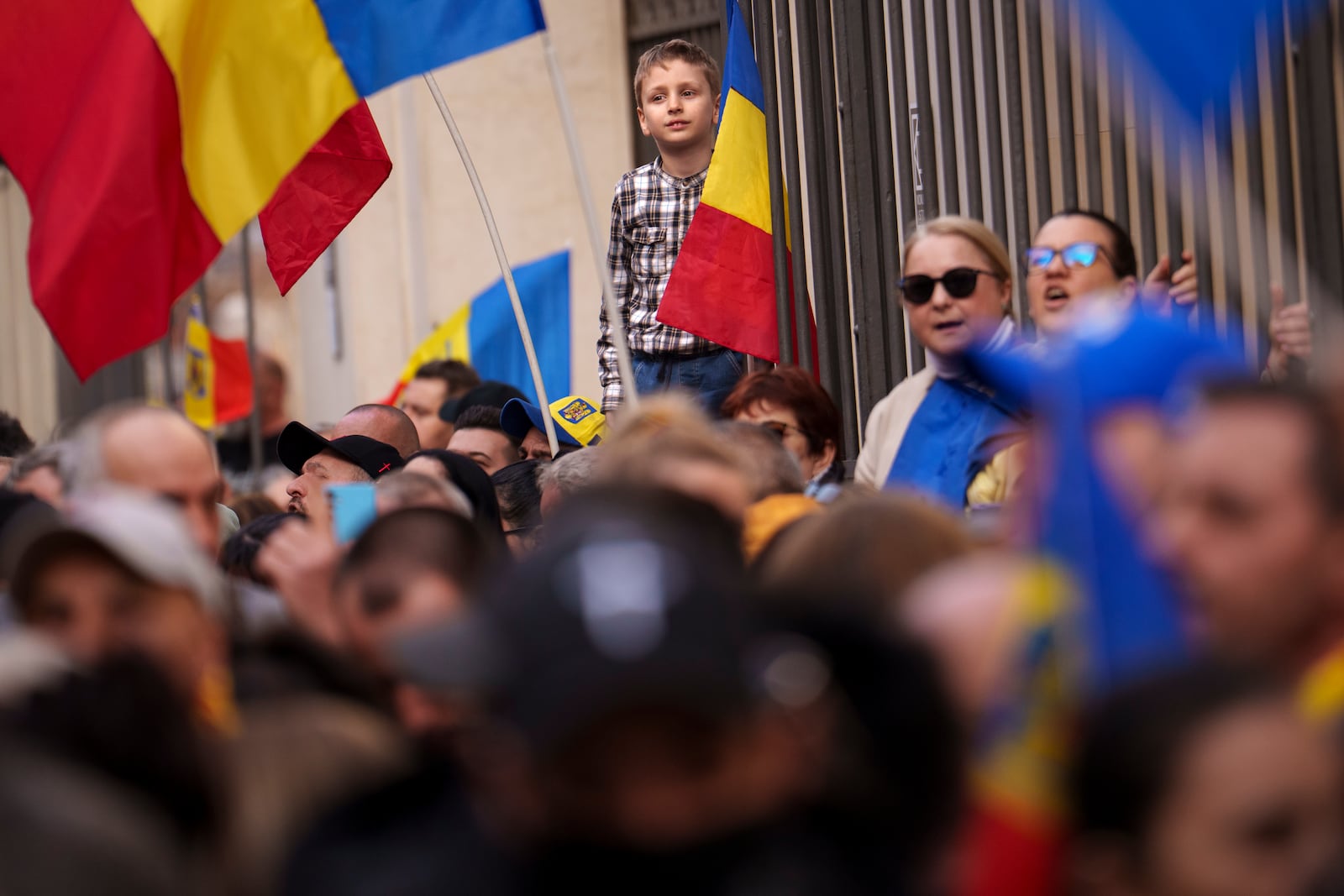 A child stands on a fence above supporters of Calin Georgescu, the winner of the first round of presidential elections, later annulled by the Constitutional Court, gathered to see him register a new bid for the country's presidency outside Romania's Electoral Authority, in Bucharest, Romania, Friday, March 7, 2025. (AP Photo/Vadim Ghirda)