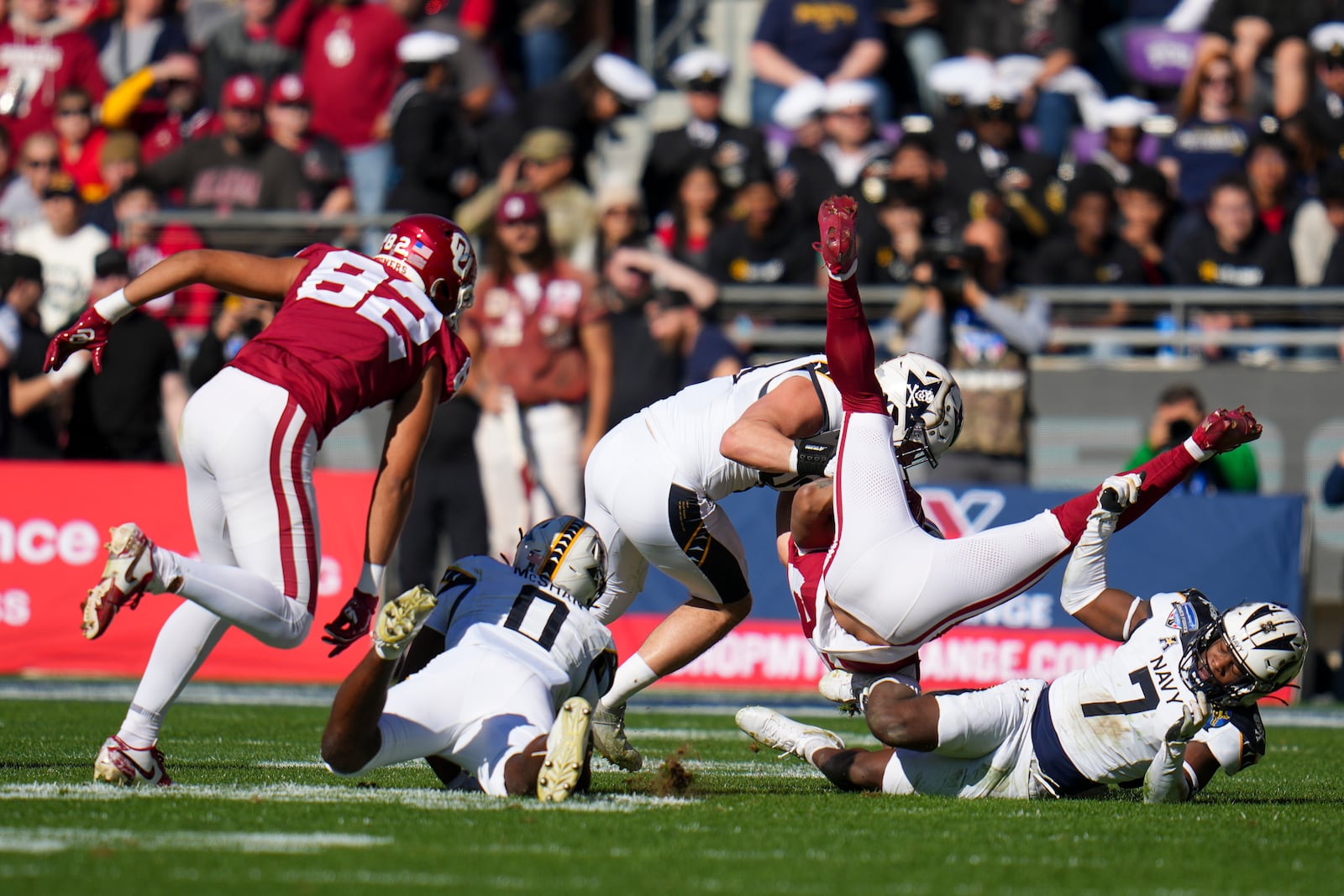 Oklahoma running back Gavin Sawchuk, second from right, is upended by Navy linebacker Mbiti Williams Jr. (7) and linebacker Kyle Jacob, center, during the first half of the Armed Forces Bowl NCAA college football game, Friday, Dec. 27, 2024, in Fort Worth, Texas. (AP Photo/Julio Cortez)