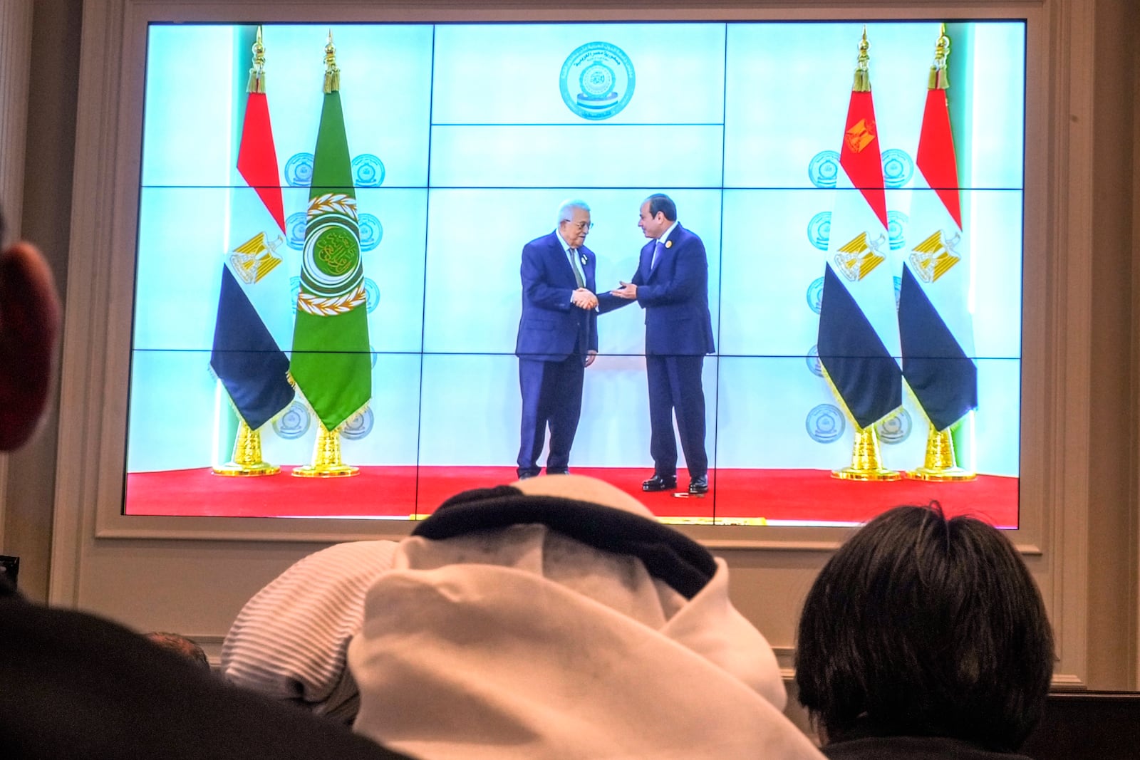 Arab reporters watch a screen displaying Egyptian President Abdel Fattah el-Sissi, right, receiving Palestinian Authority President Mahmoud Abbas, at the press center hall of the emergency Arab summit at Egypt's New Administrative Capital, just outside Cairo, Tuesday, March 4, 2025. (AP Photo/Amr Nabil)